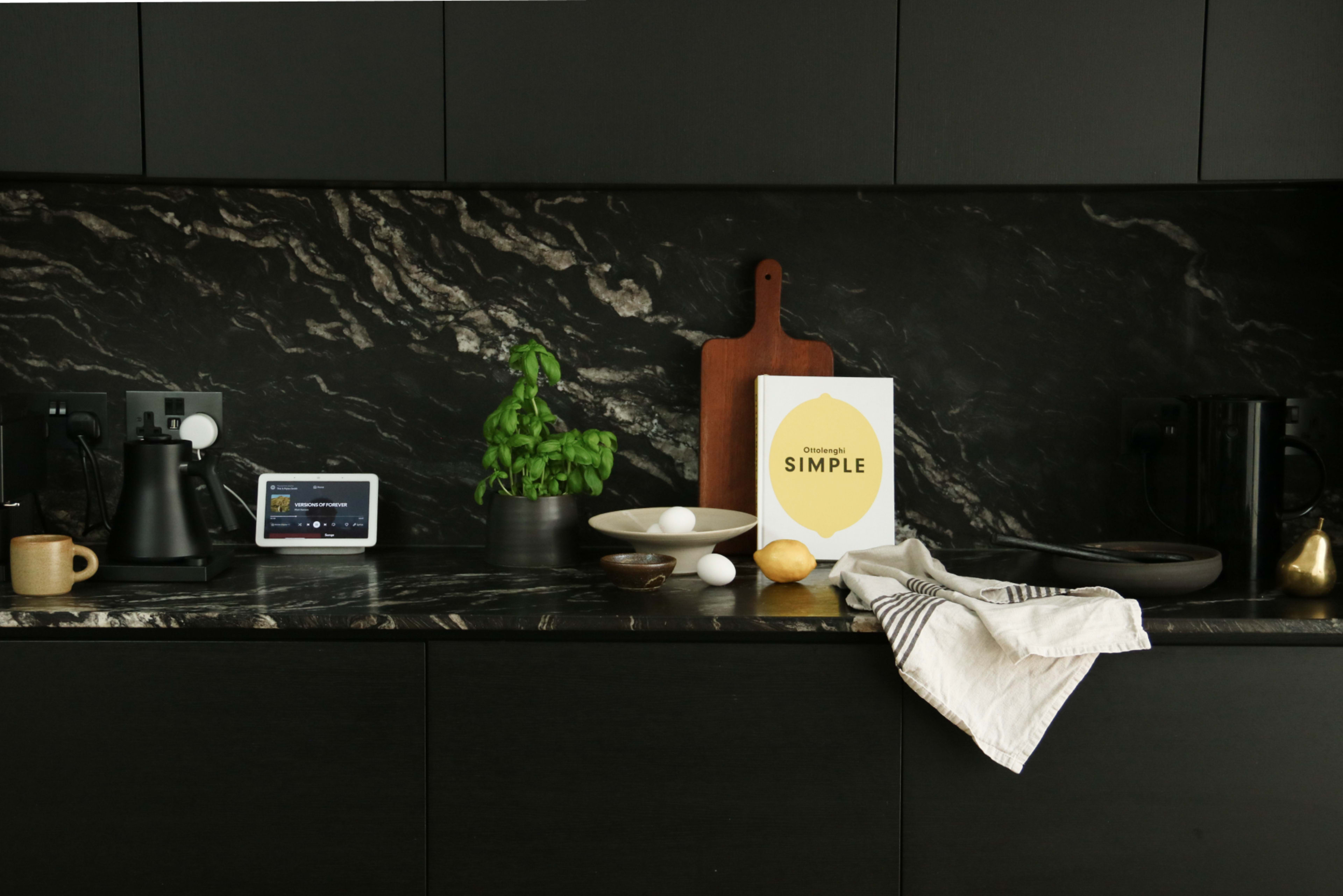 The image features a modern kitchen countertop with dark marble, a tablet displaying content, fresh basil, cooking utensils, a bowl with an egg and a lemon, and a cookbook titled "SIMPLE."