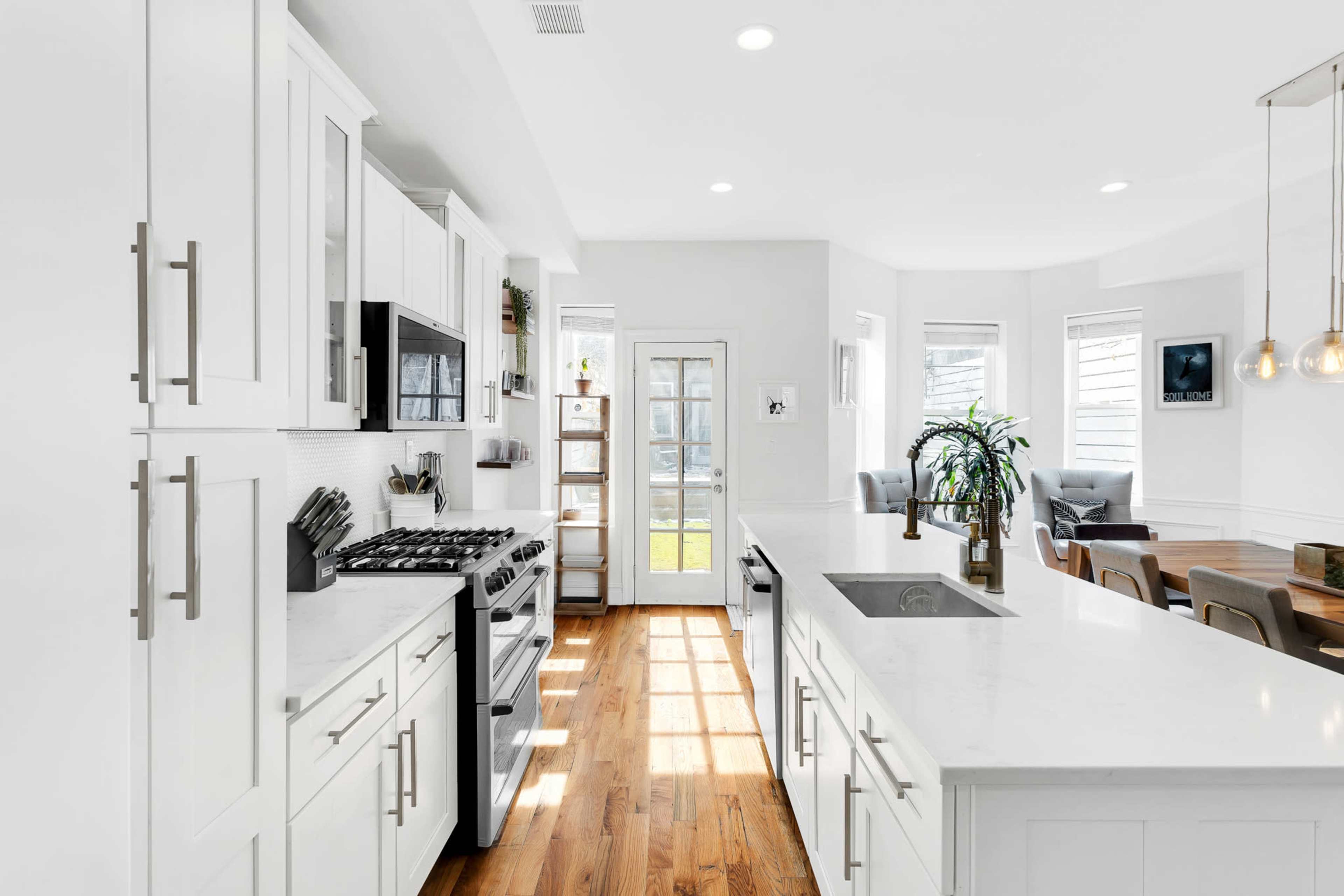 A modern kitchen with white cabinets, a stainless steel gas stove, and a view of a dining area through a glass door.
