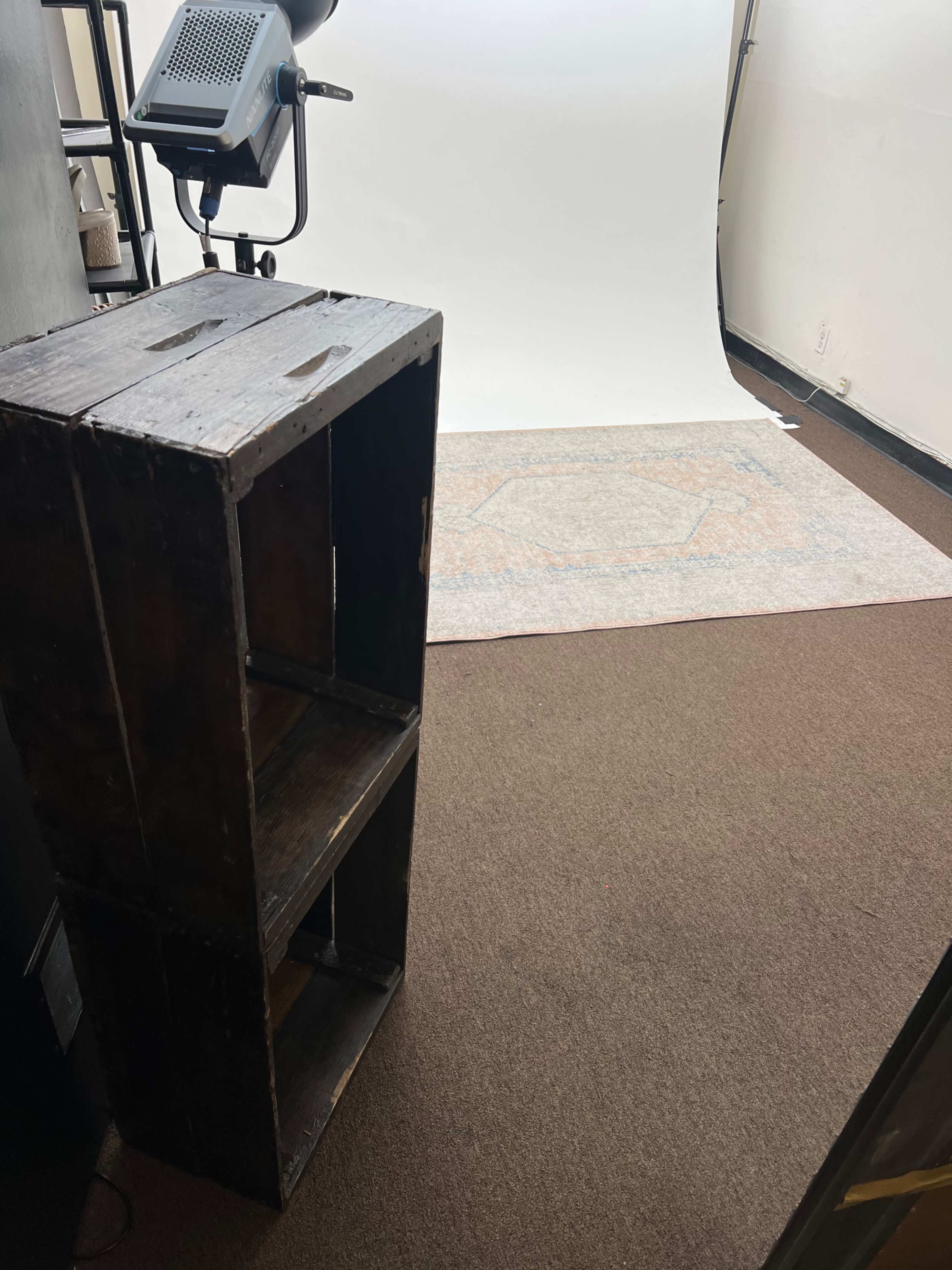 The image shows a wooden crate positioned beside a light source, with a white backdrop and patterned rug in the background.