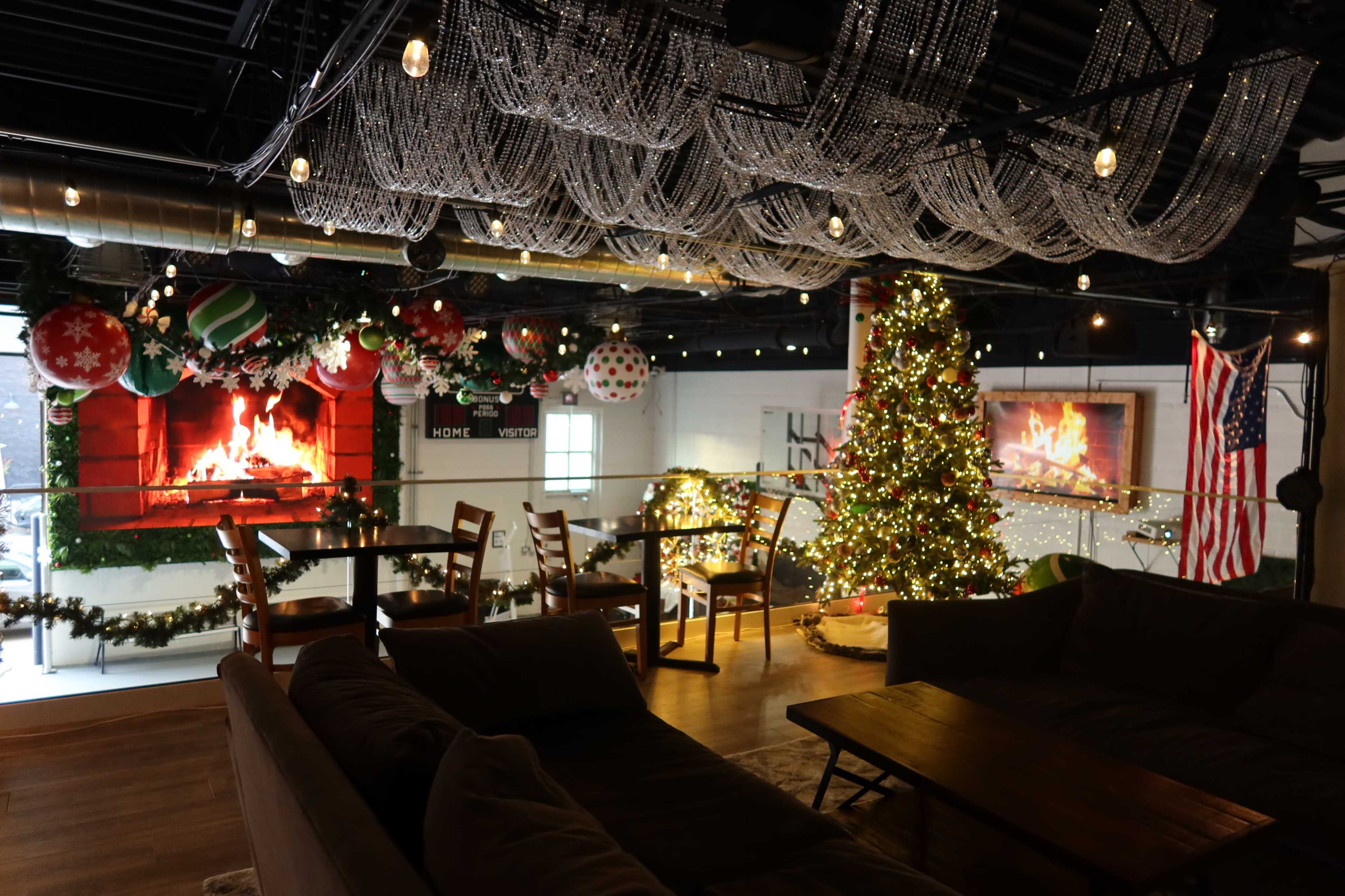 The scene depicts a festive indoor space decorated for the holidays, featuring a Christmas tree, ornaments, string lights, and a couple of artificial fireplaces.