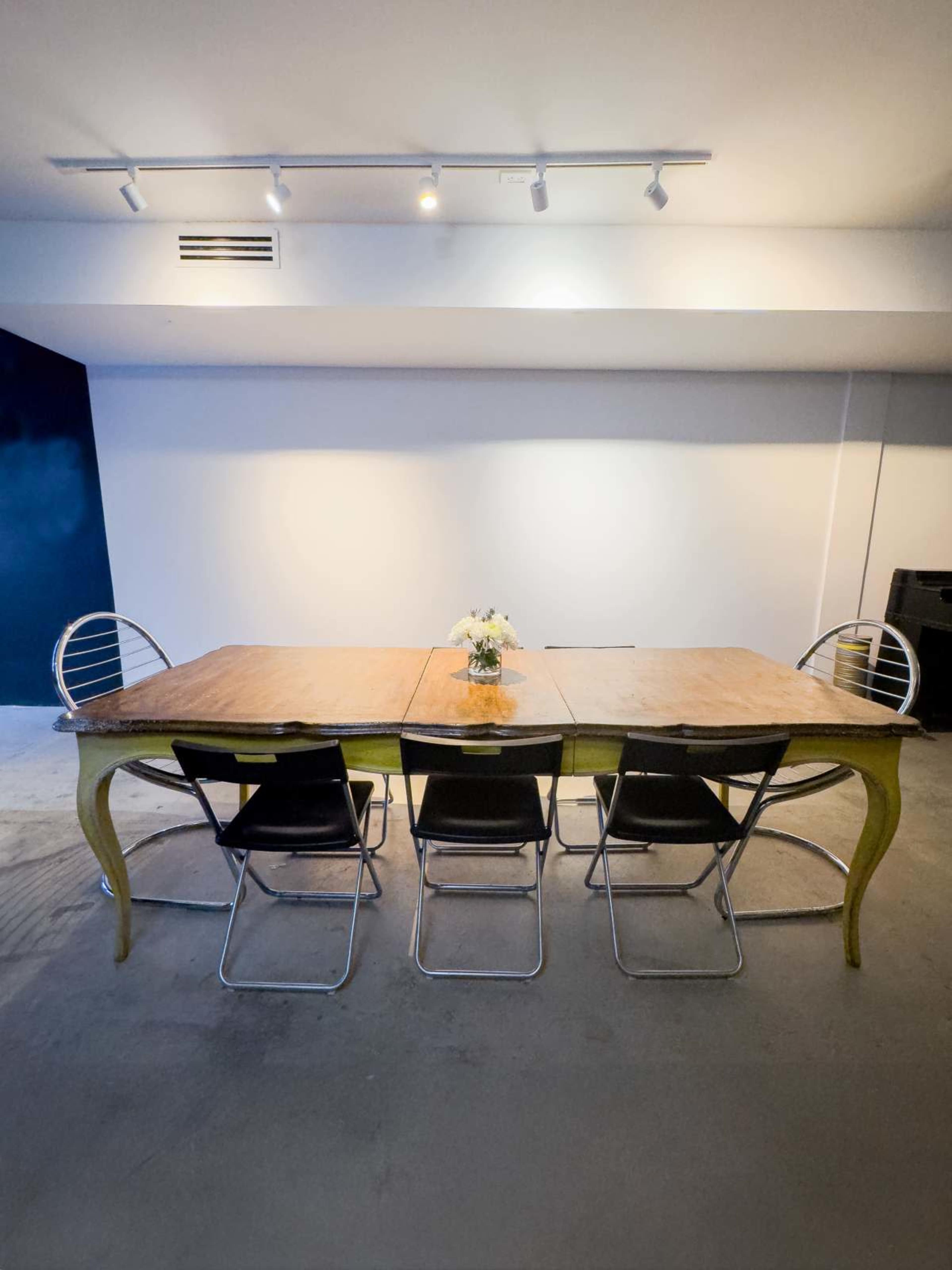 A long wooden table with a vase of flowers is set in a room featuring four black chairs arranged around it.