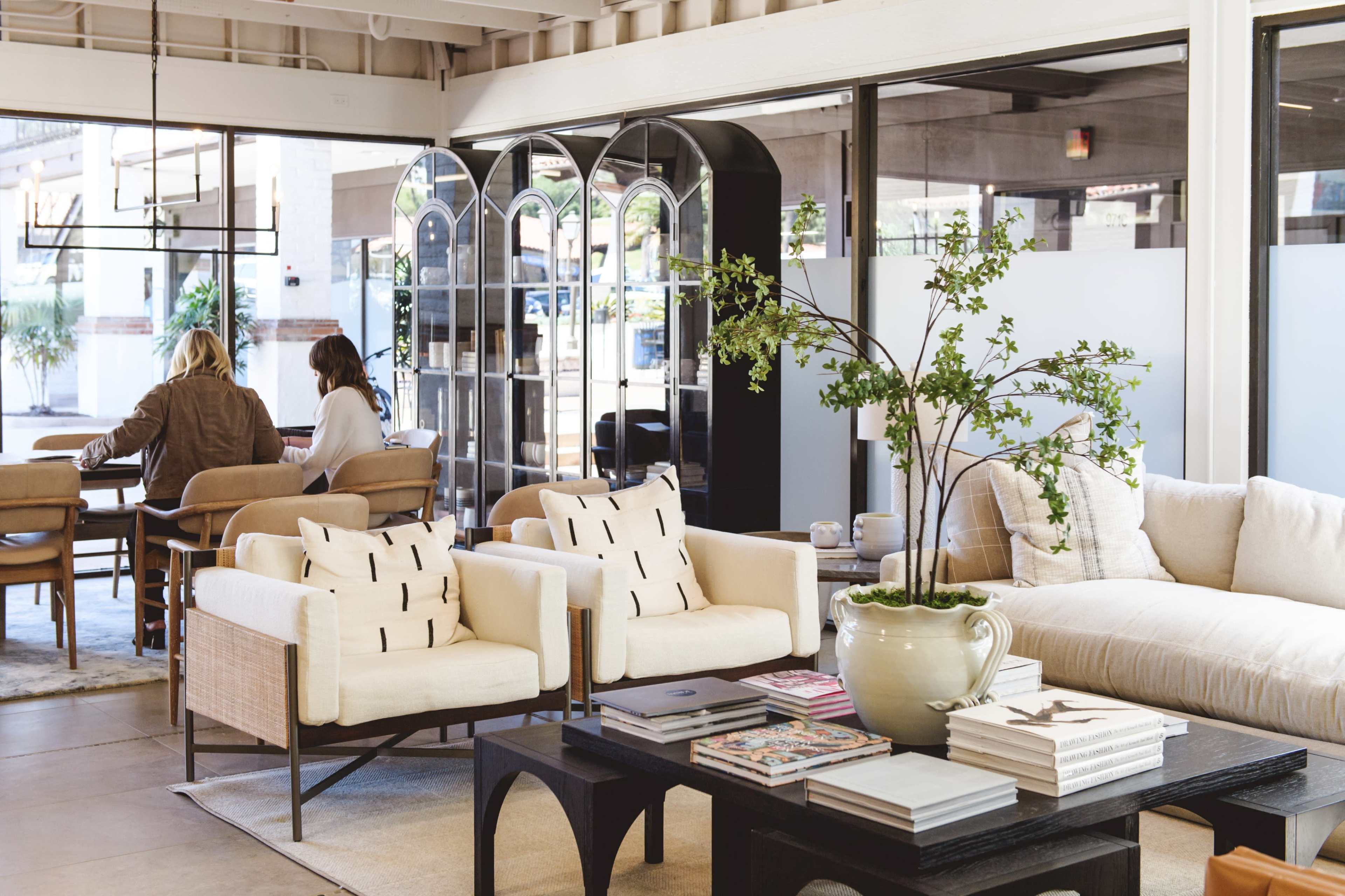 A modern interior space with a seating area featuring light chairs and a coffee table, alongside a dining area in the background.