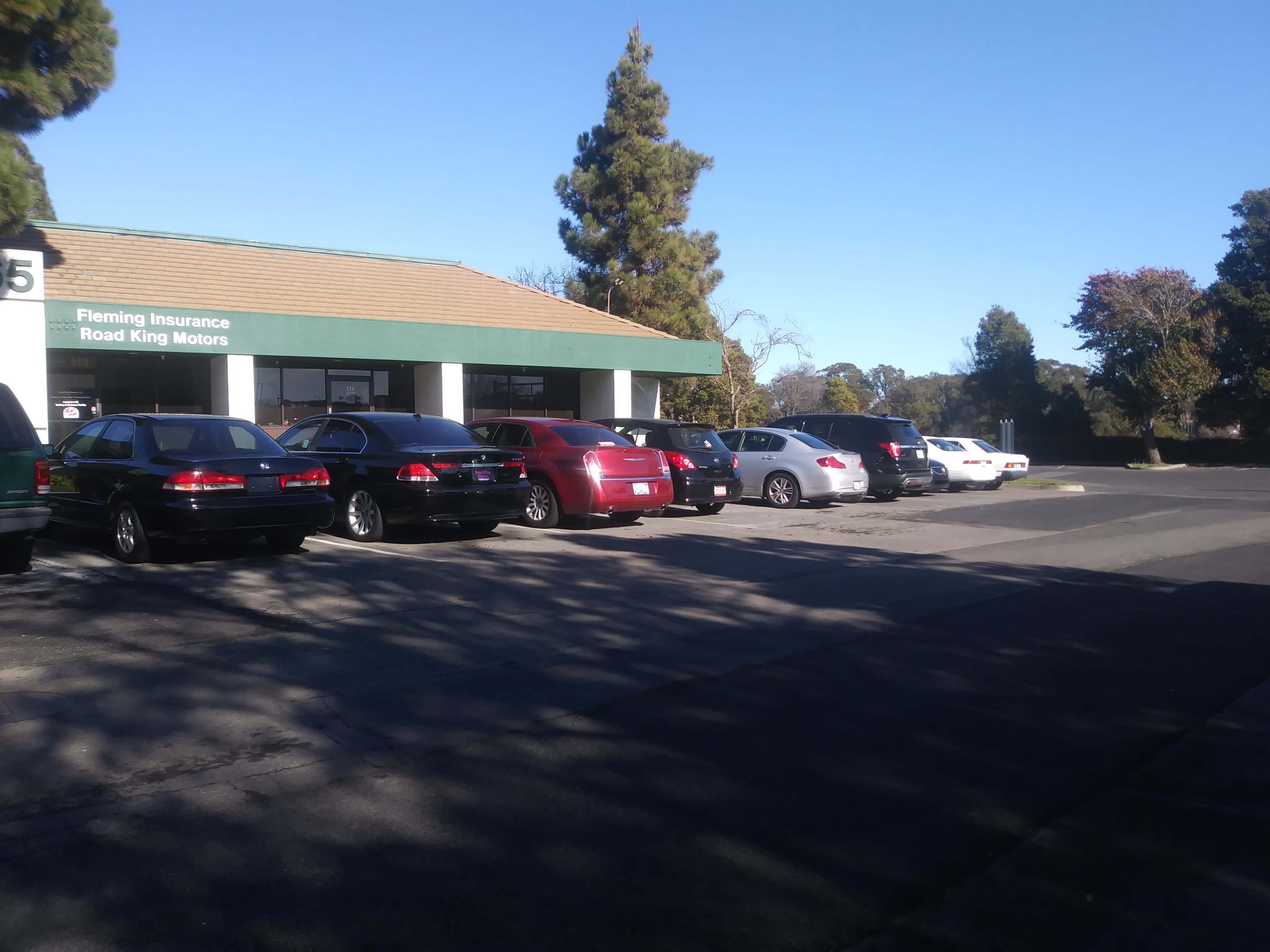 A row of parked cars is lined up in front of a building with a sign for Fleming Insurance and Road King Motors.