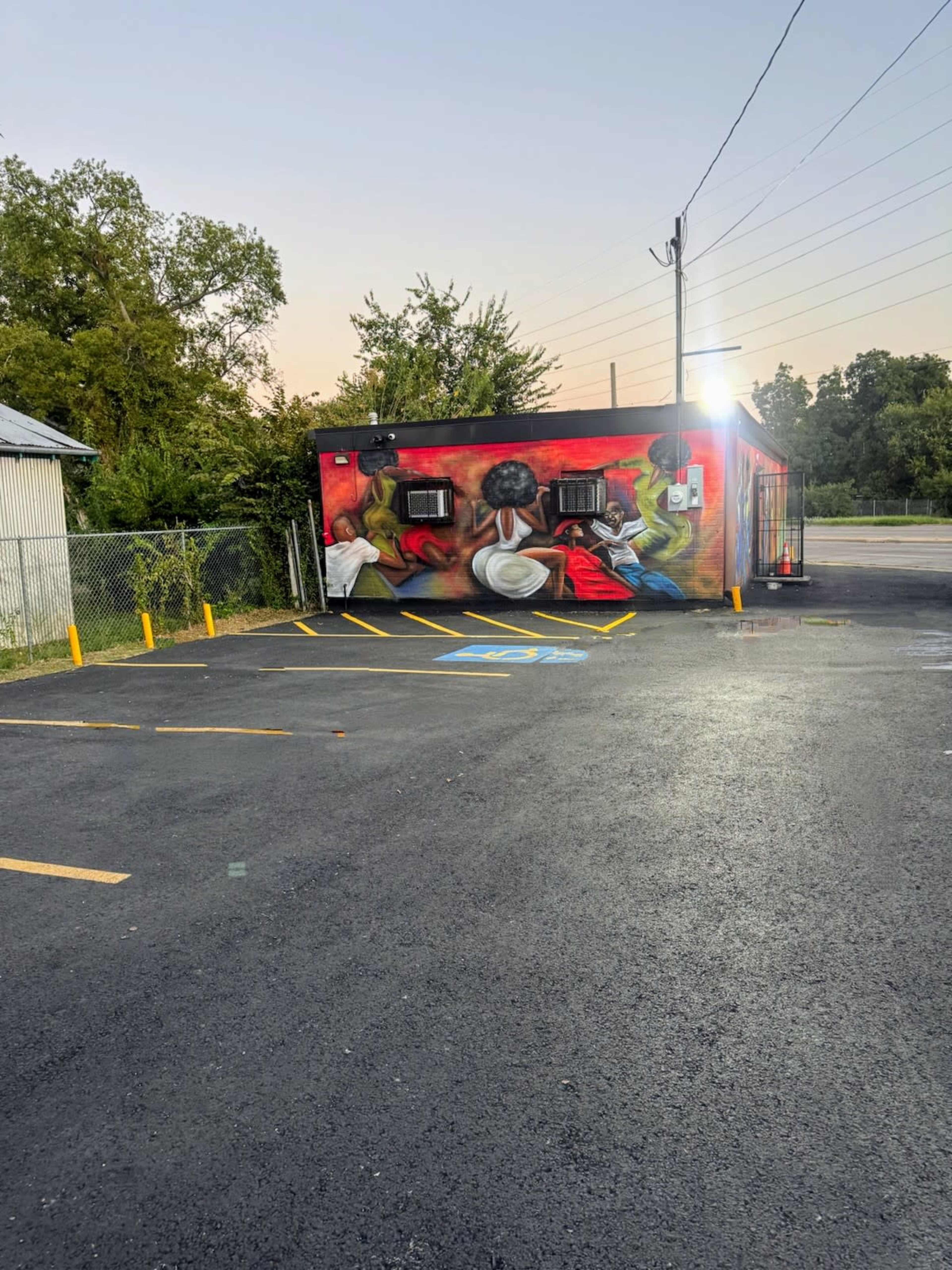 A brightly painted mural depicting people engaged in various activities adorns the side of a small building next to a parking lot.