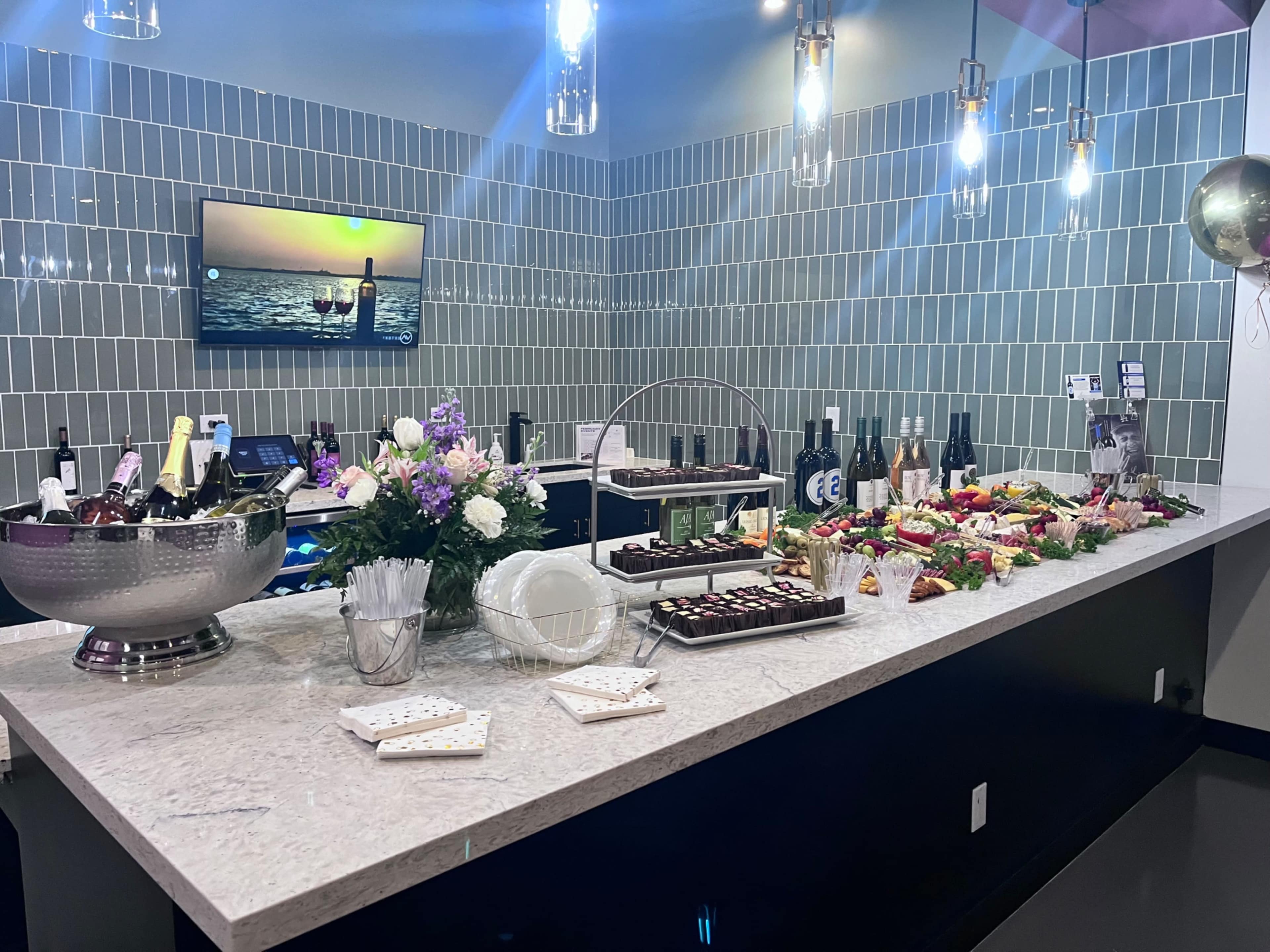 A buffet table is set up with a variety of food items, drinks, and decorative flowers in a well-lit room.
