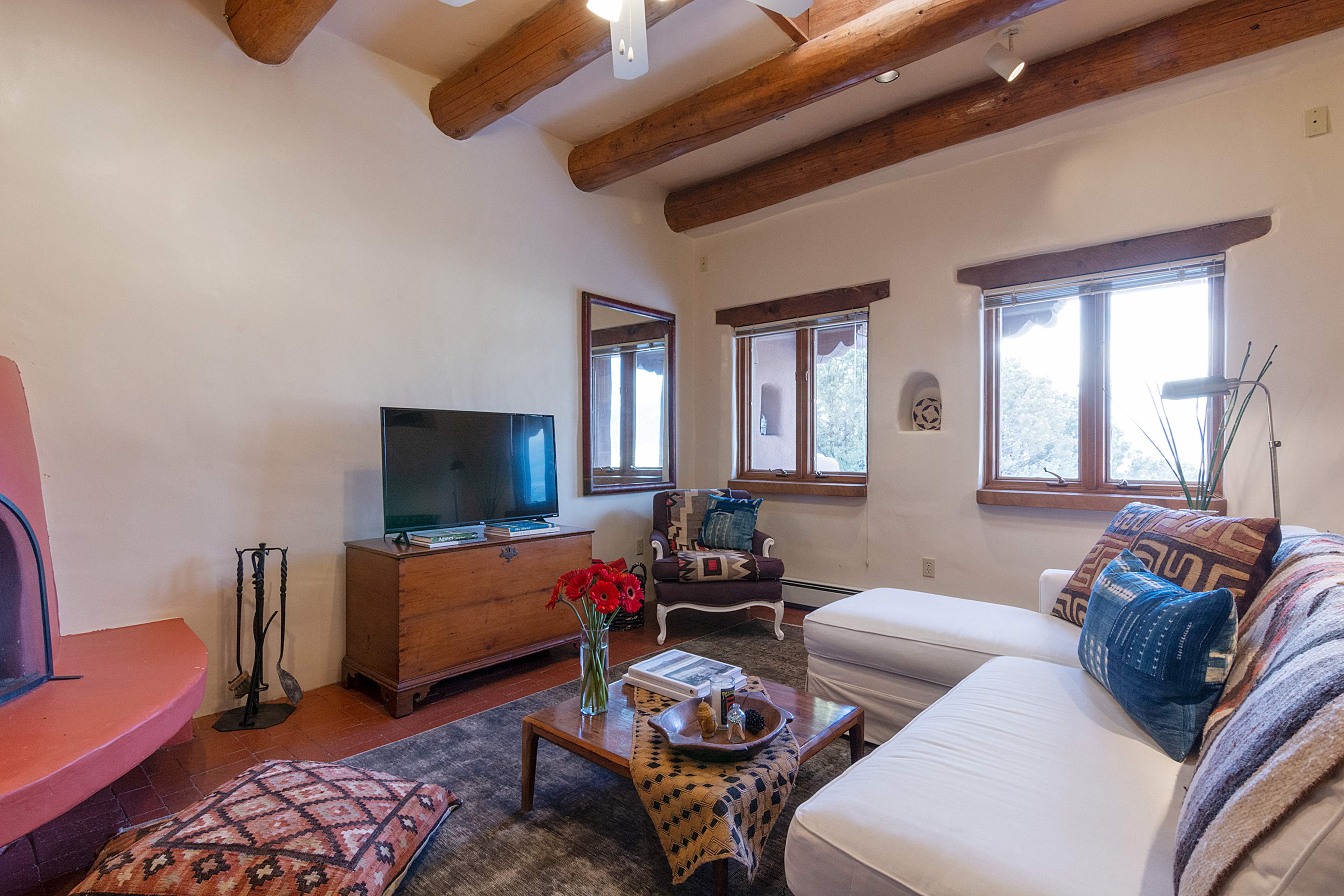 The room features a white sofa, a wooden coffee table with a decorative bowl, a television, and a fireplace, surrounded by windows that provide natural light.
