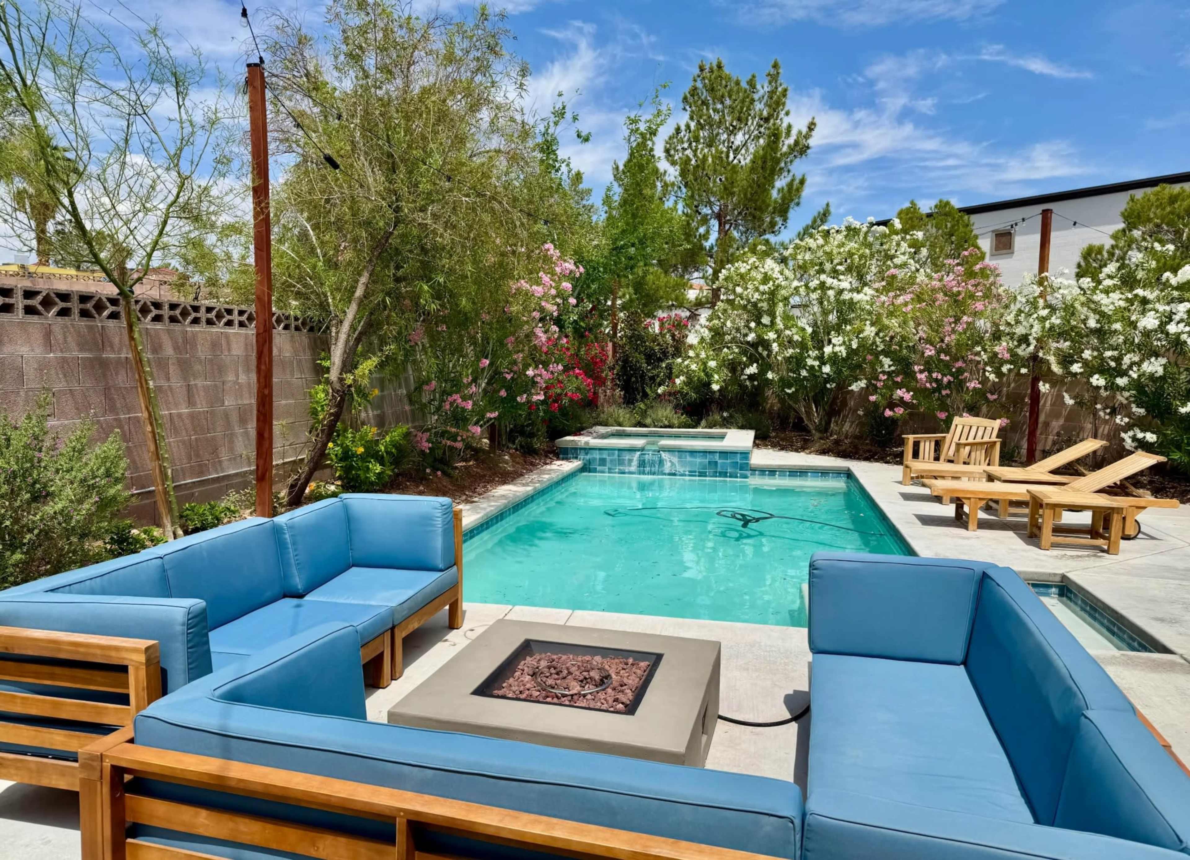 A backyard features a swimming pool surrounded by stylish seating and colorful flowering plants.