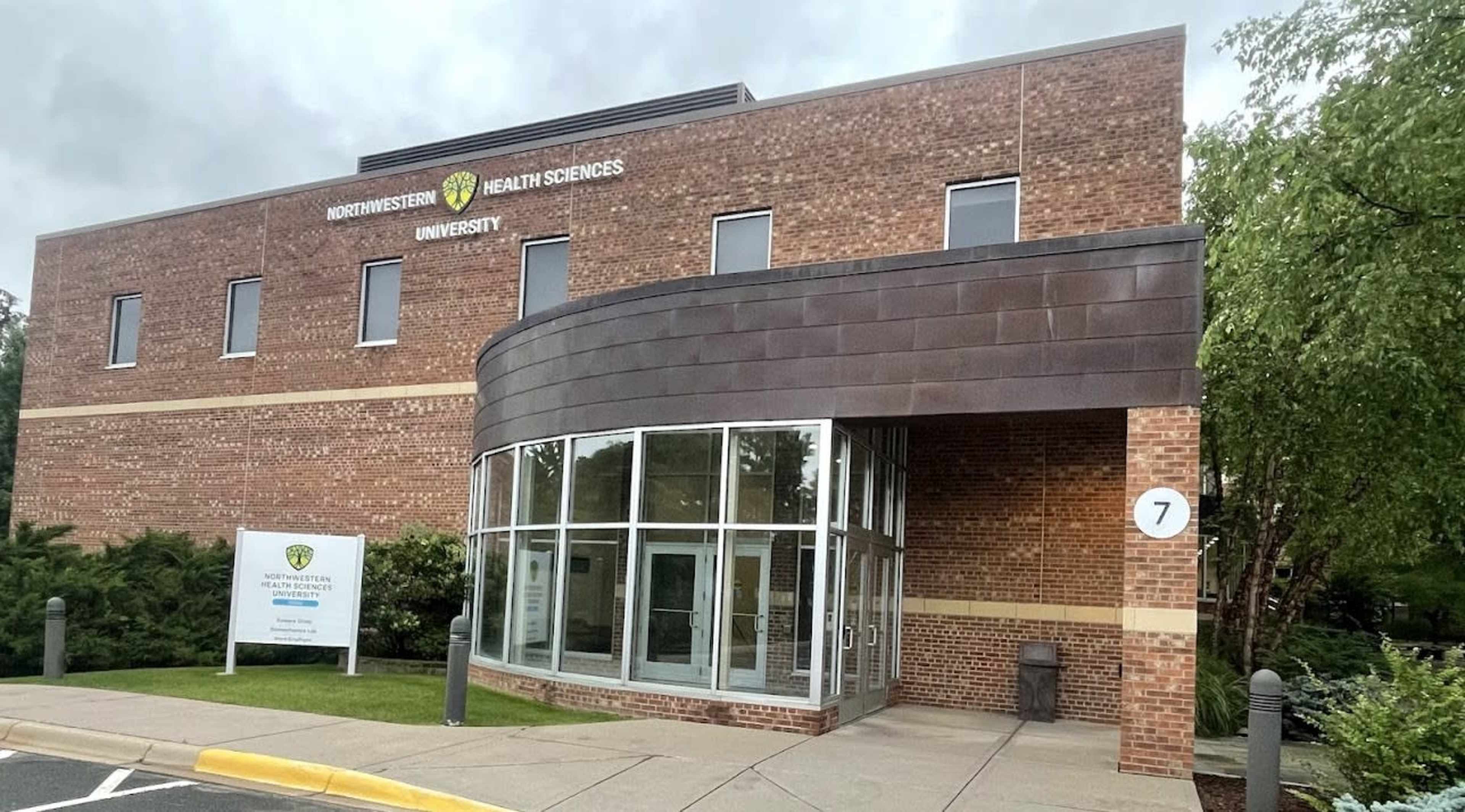 The entrance of Northwestern Health Sciences University, featuring a brick building with large glass doors and a sign in front.