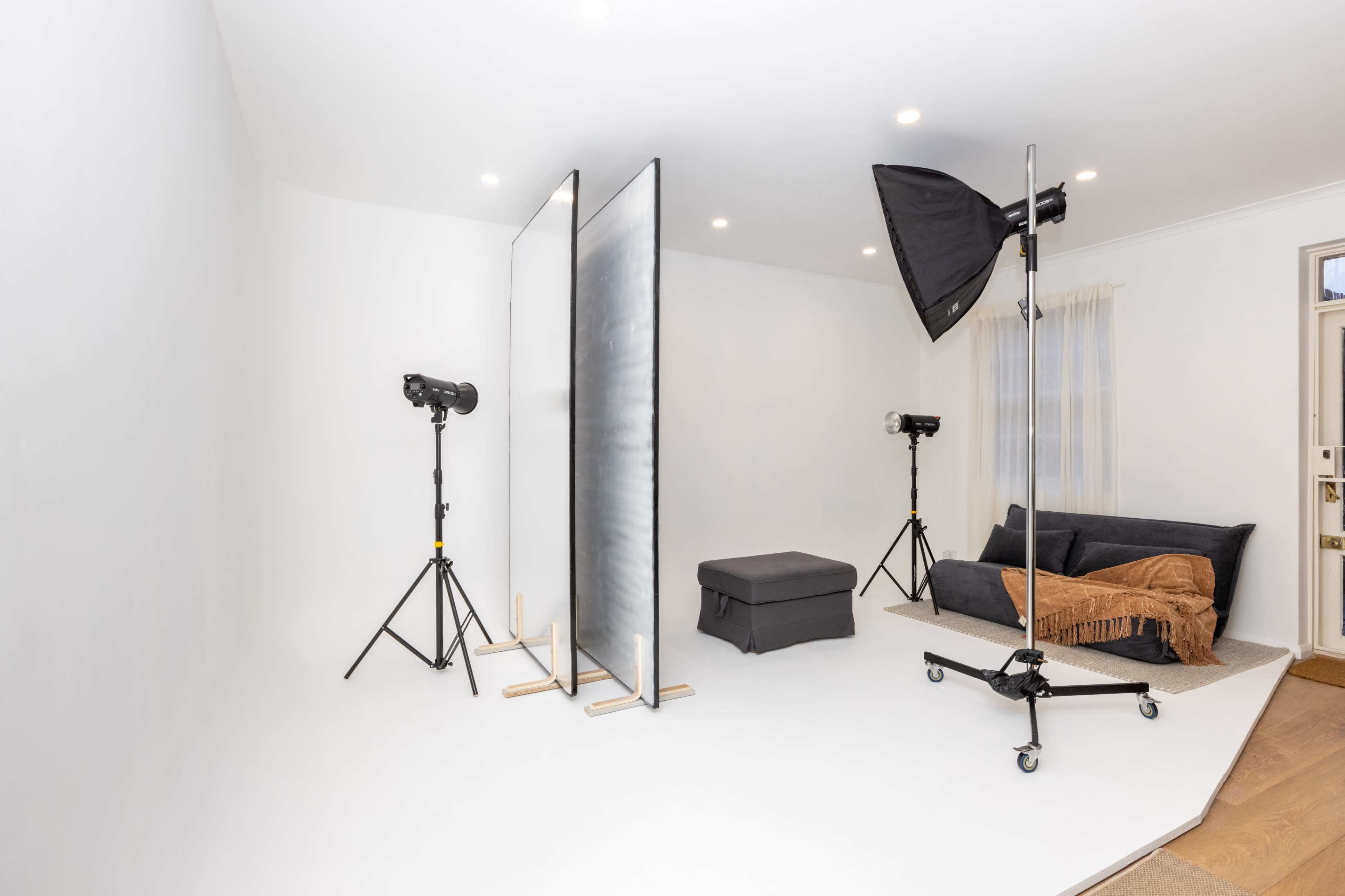 A minimalist photography studio with a gray couch, two softbox lights on stands, and a backdrop setup.