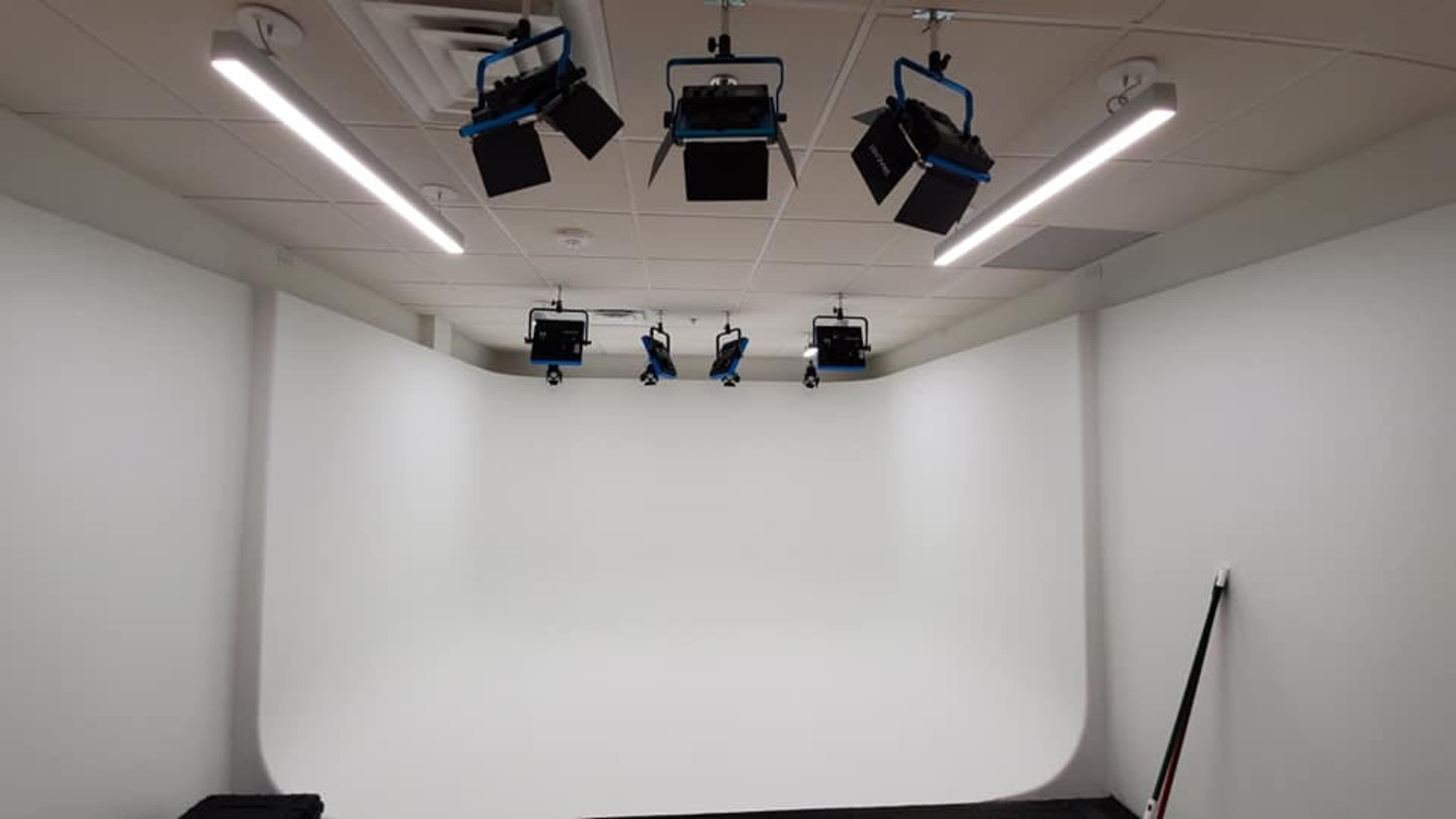 A photo studio with a seamless white backdrop and multiple overhead lights mounted on the ceiling.