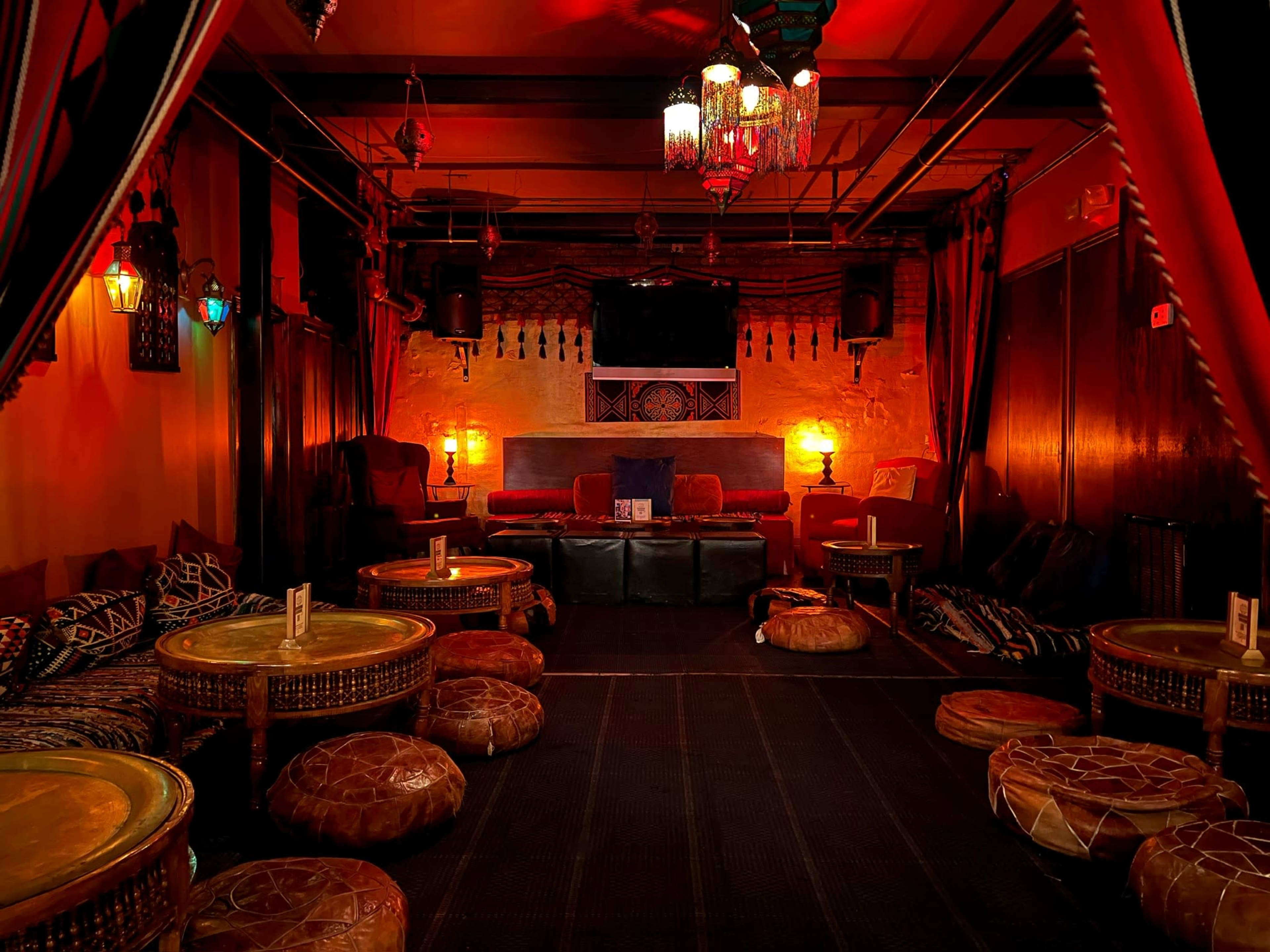 A dimly lit lounge with low seating, ornate lanterns, and decorative fabrics lining the walls.