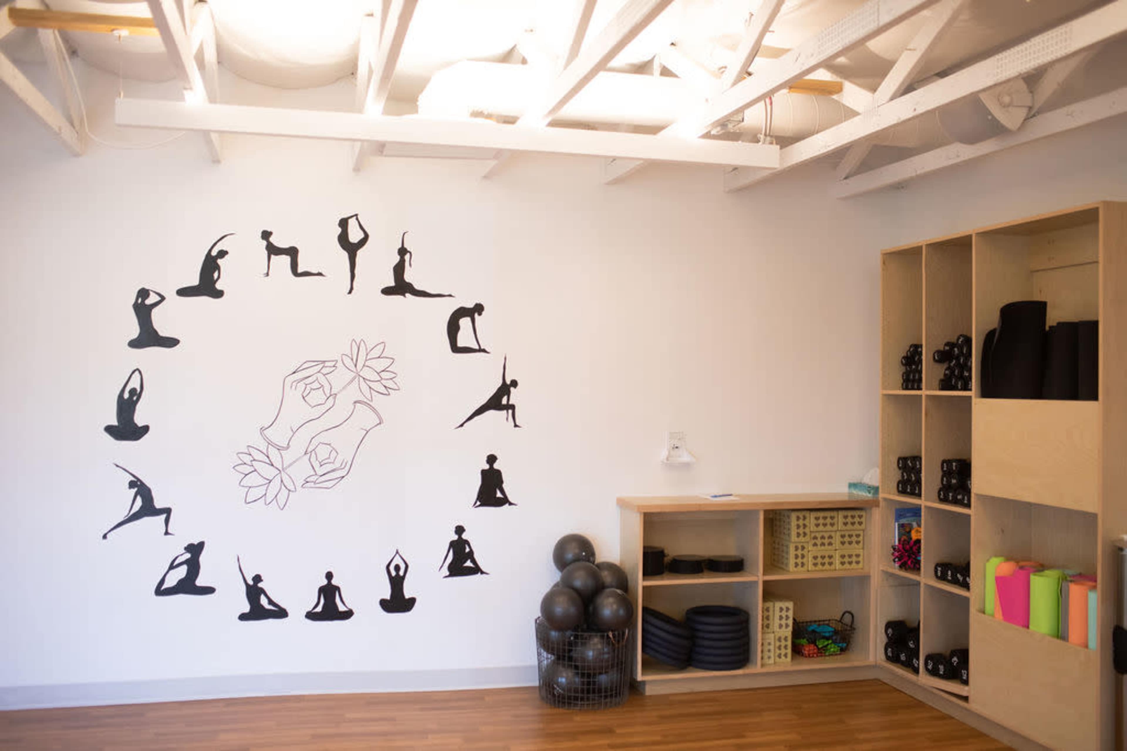 A yoga studio with a wall mural depicting various yoga poses and a shelf stocked with fitness equipment.