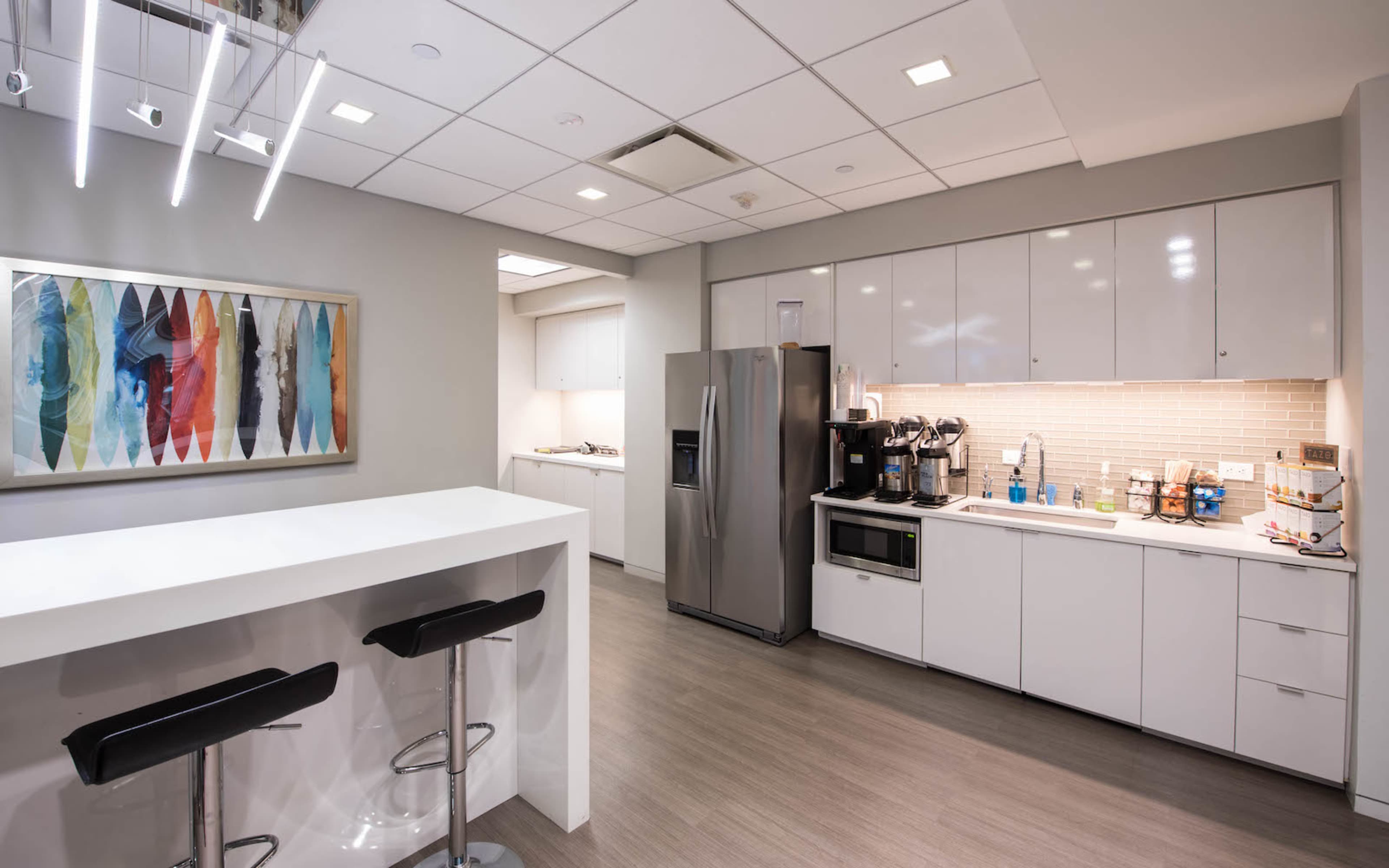 A modern kitchen with a countertop bar, stainless steel appliances, and light-colored cabinetry.