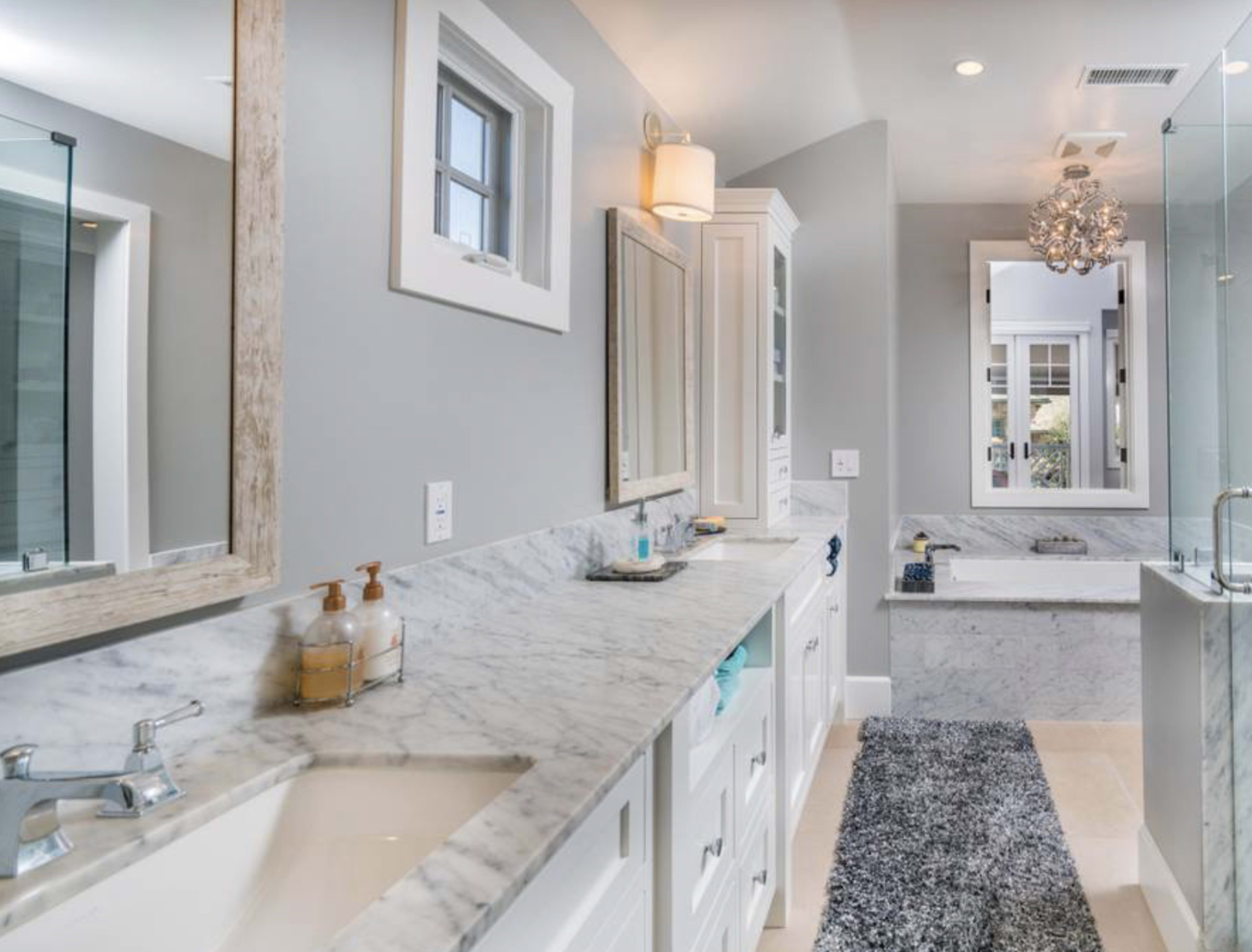 The image shows a modern bathroom featuring a double sink vanity with marble countertops, a glass shower, and a bathtub with a marble surround.