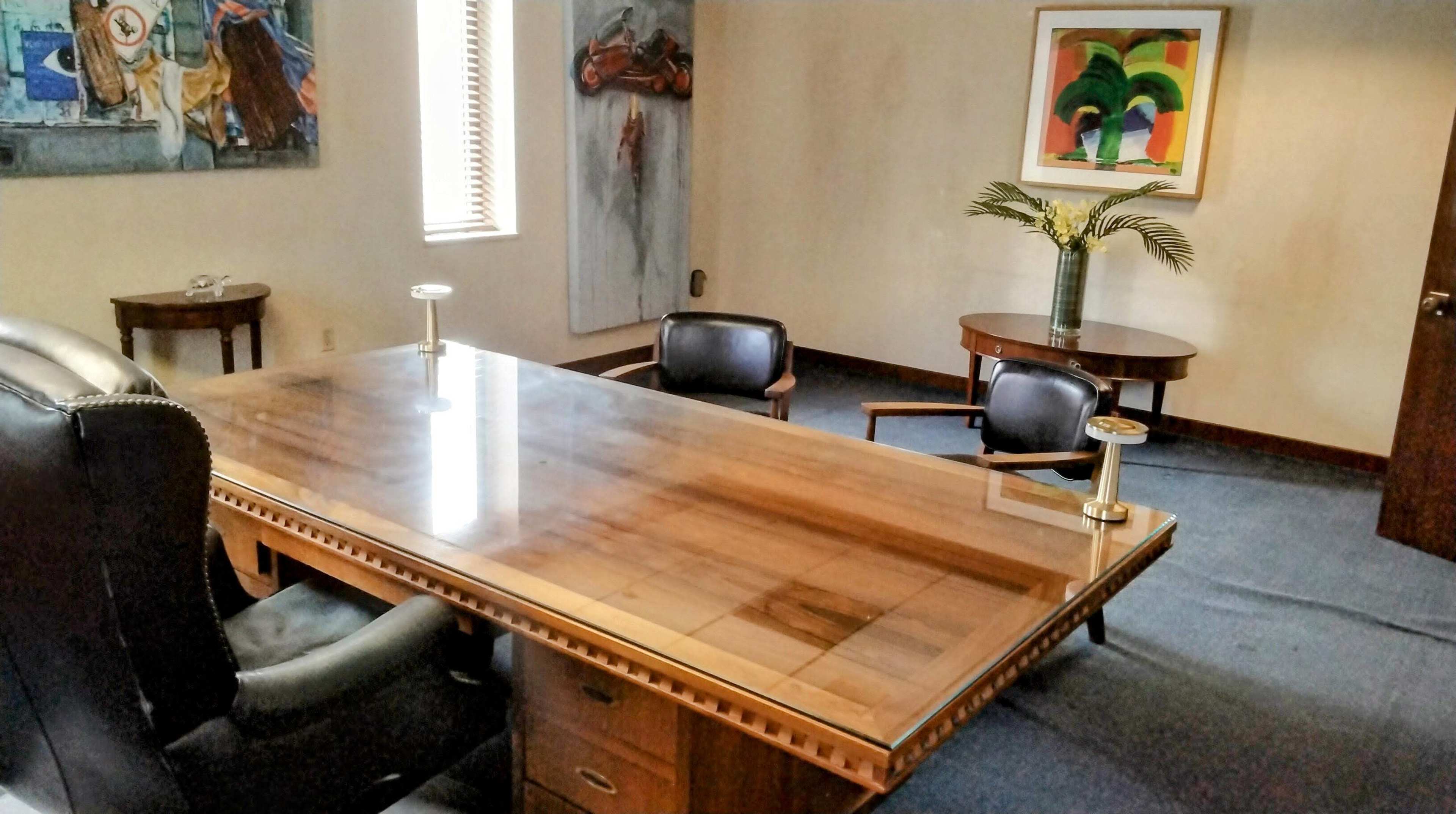The image shows a conference room with a large wooden table, two black chairs, a small round table, and paintings on the walls.