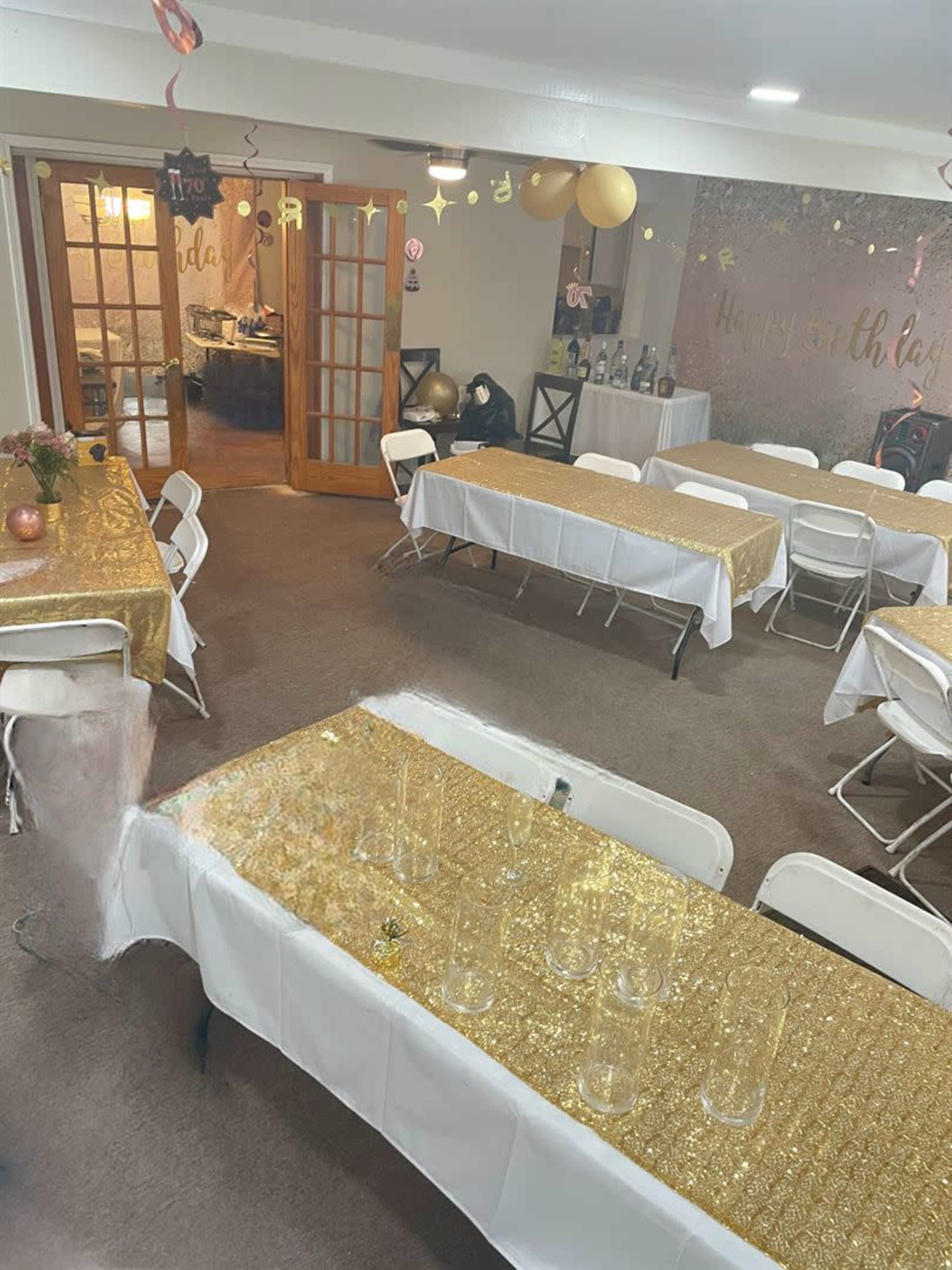 A decorated indoor party space with several tables covered in gold glitter tablecloths and a door leading to another room in the background.