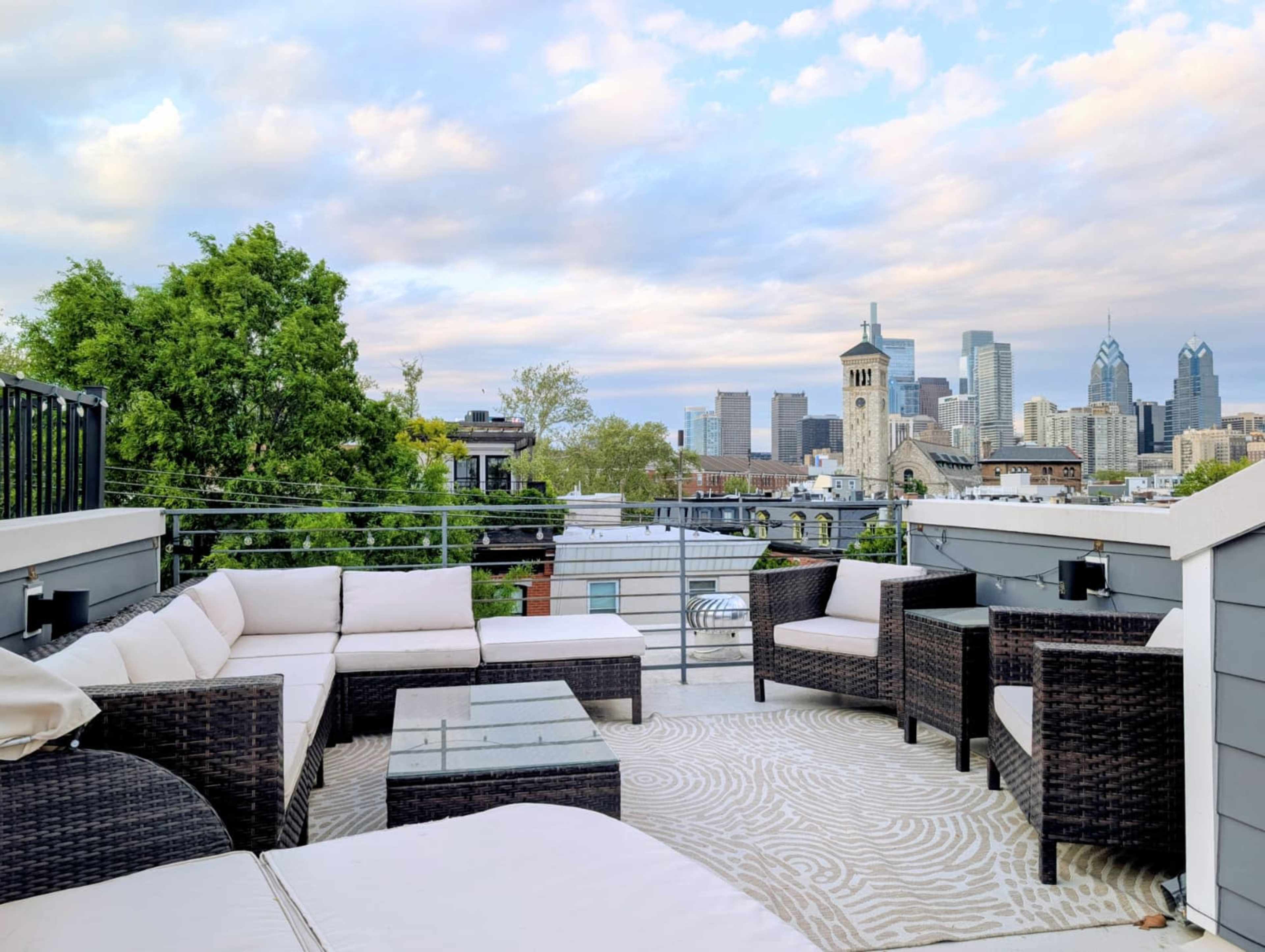 The image shows a rooftop terrace with modern furniture overlooking a city skyline.
