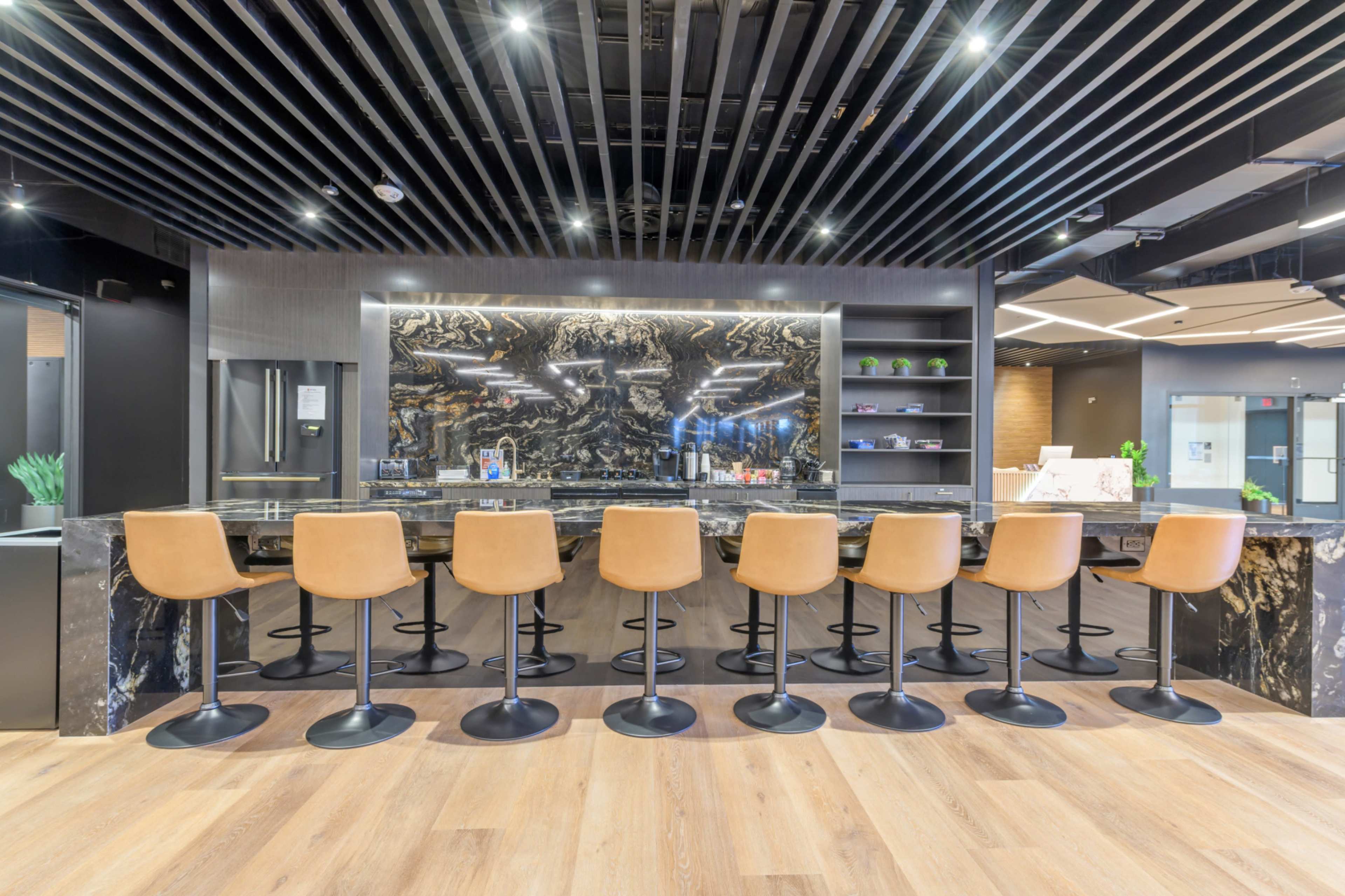 A modern bar area features a long dark countertop with brown leather stools arranged in front of a decorative black and gold backsplash.