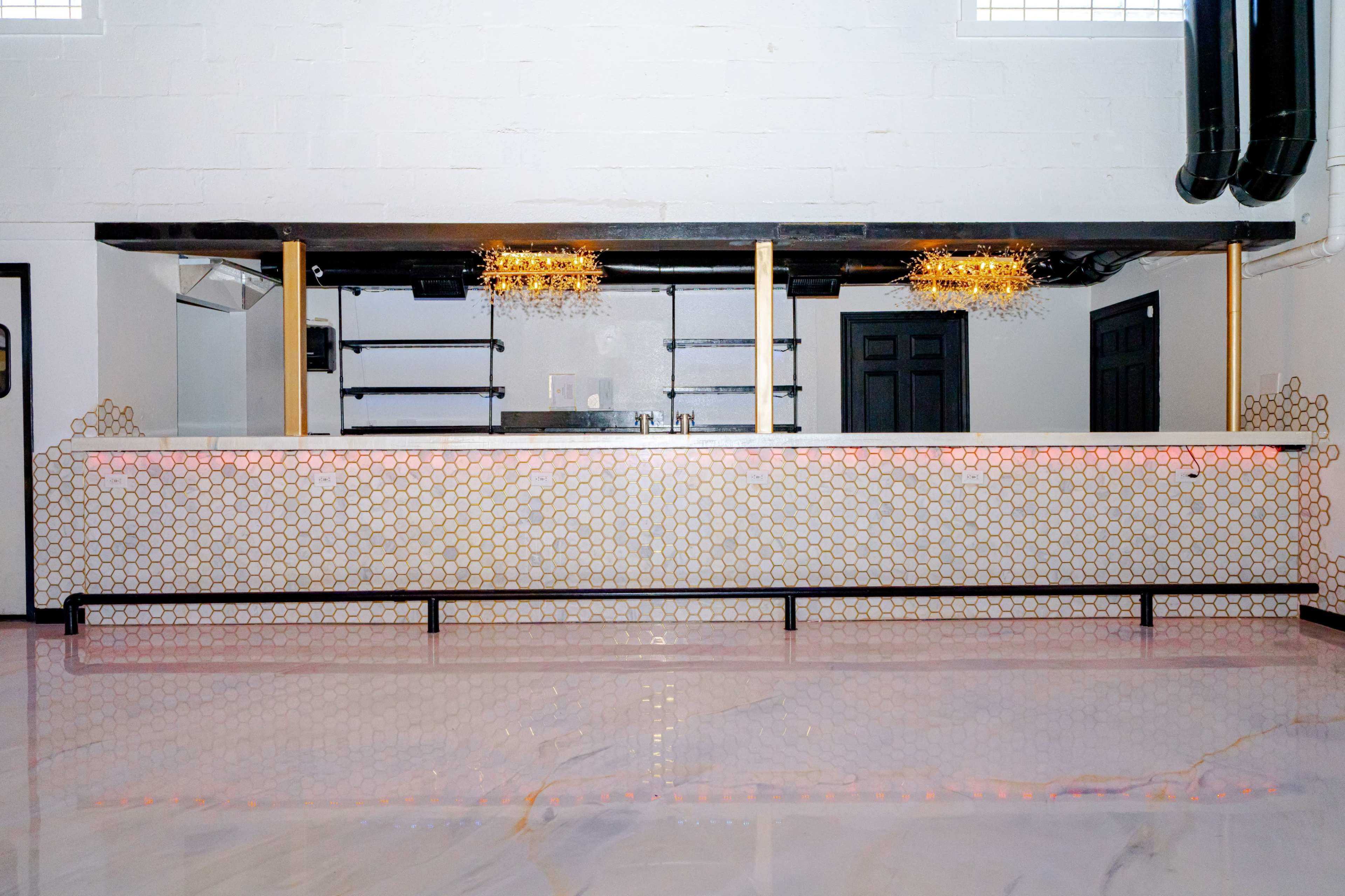 The image shows a modern bar with a marble countertop and a decorative honeycomb-patterned front, illuminated by golden light fixtures.
