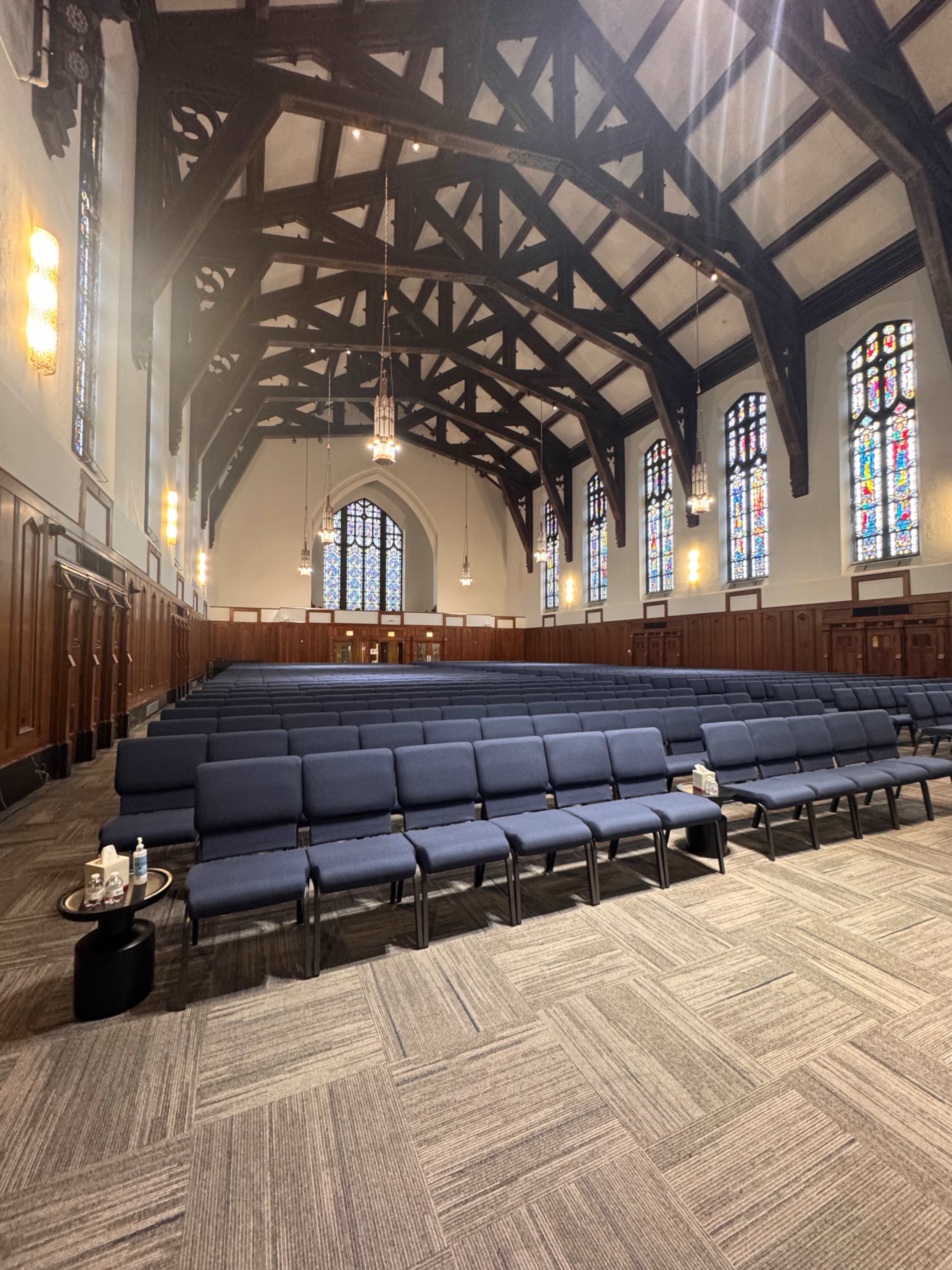The image shows a large, empty church interior with rows of blue seating and stained glass windows.