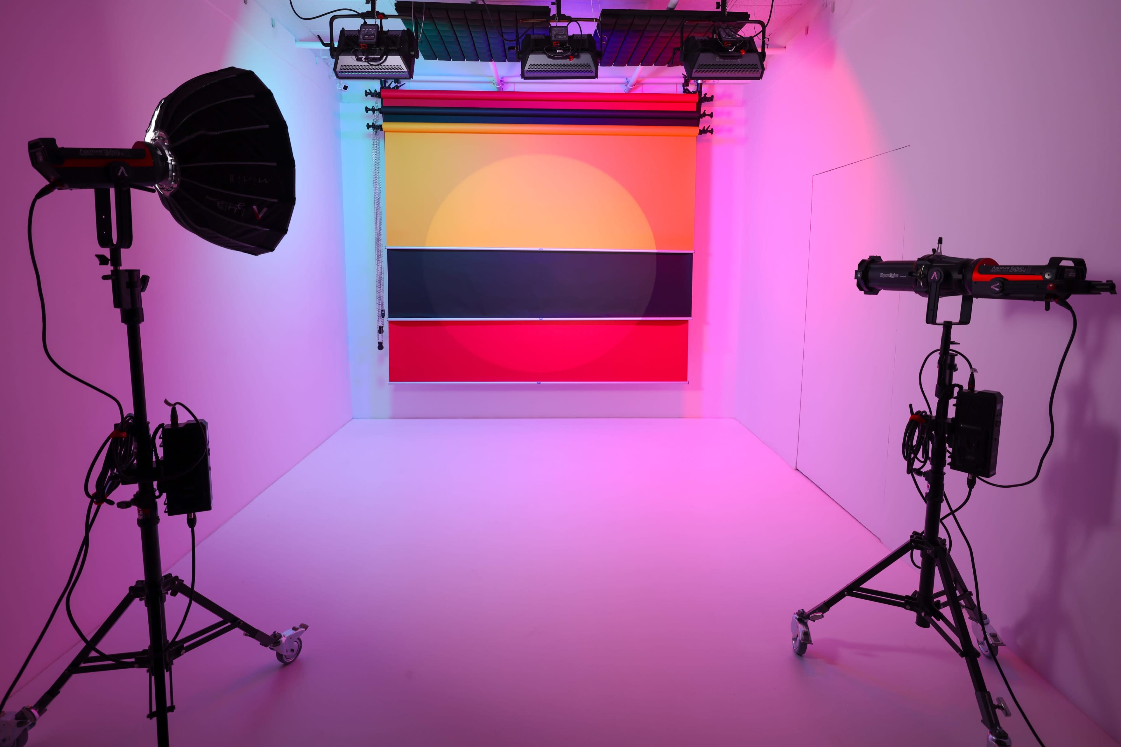 A photography studio features two lighting setups on either side of a vibrant backdrop of geometric colors.