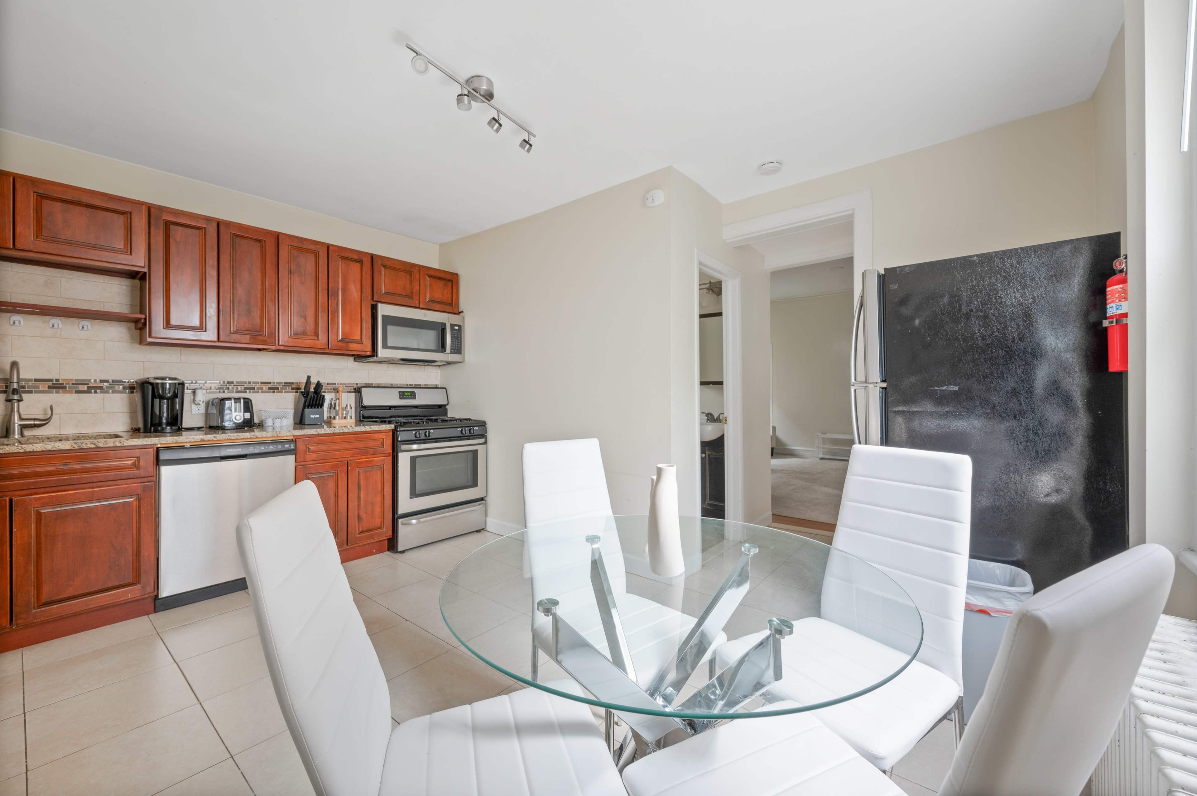A modern kitchen features wooden cabinets, stainless steel appliances, and a glass dining table with white chairs.