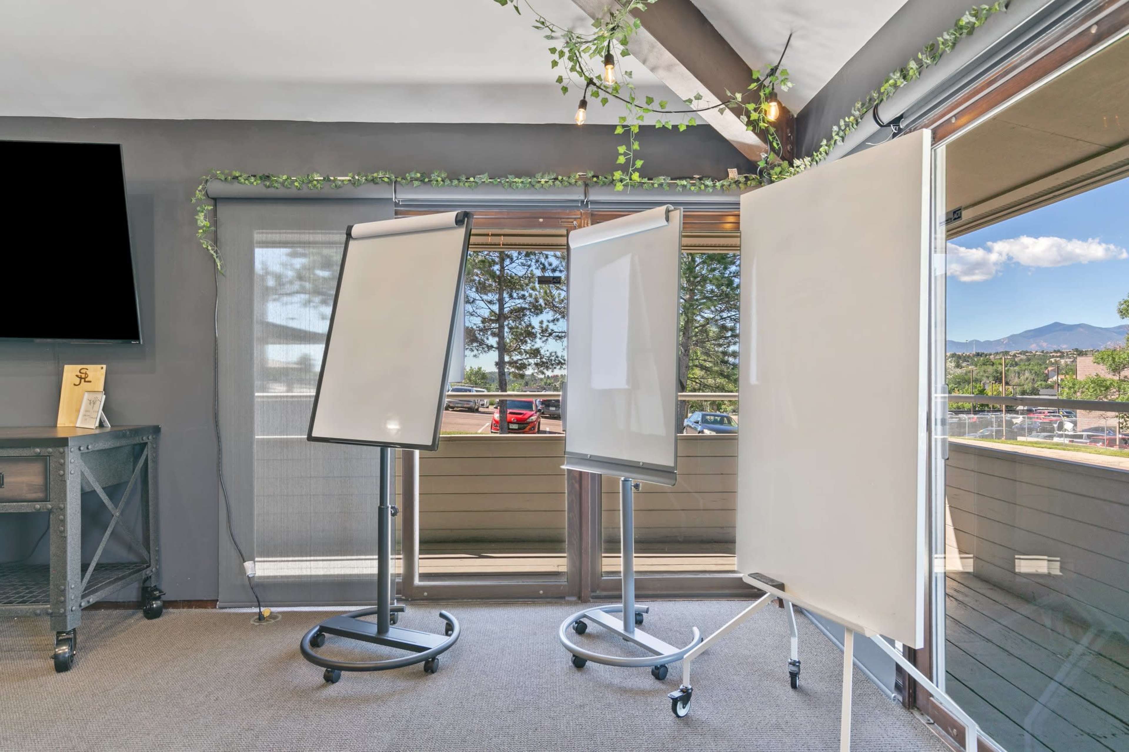 A room with three whiteboards on stands, overlooking a view of trees and mountains through large windows.