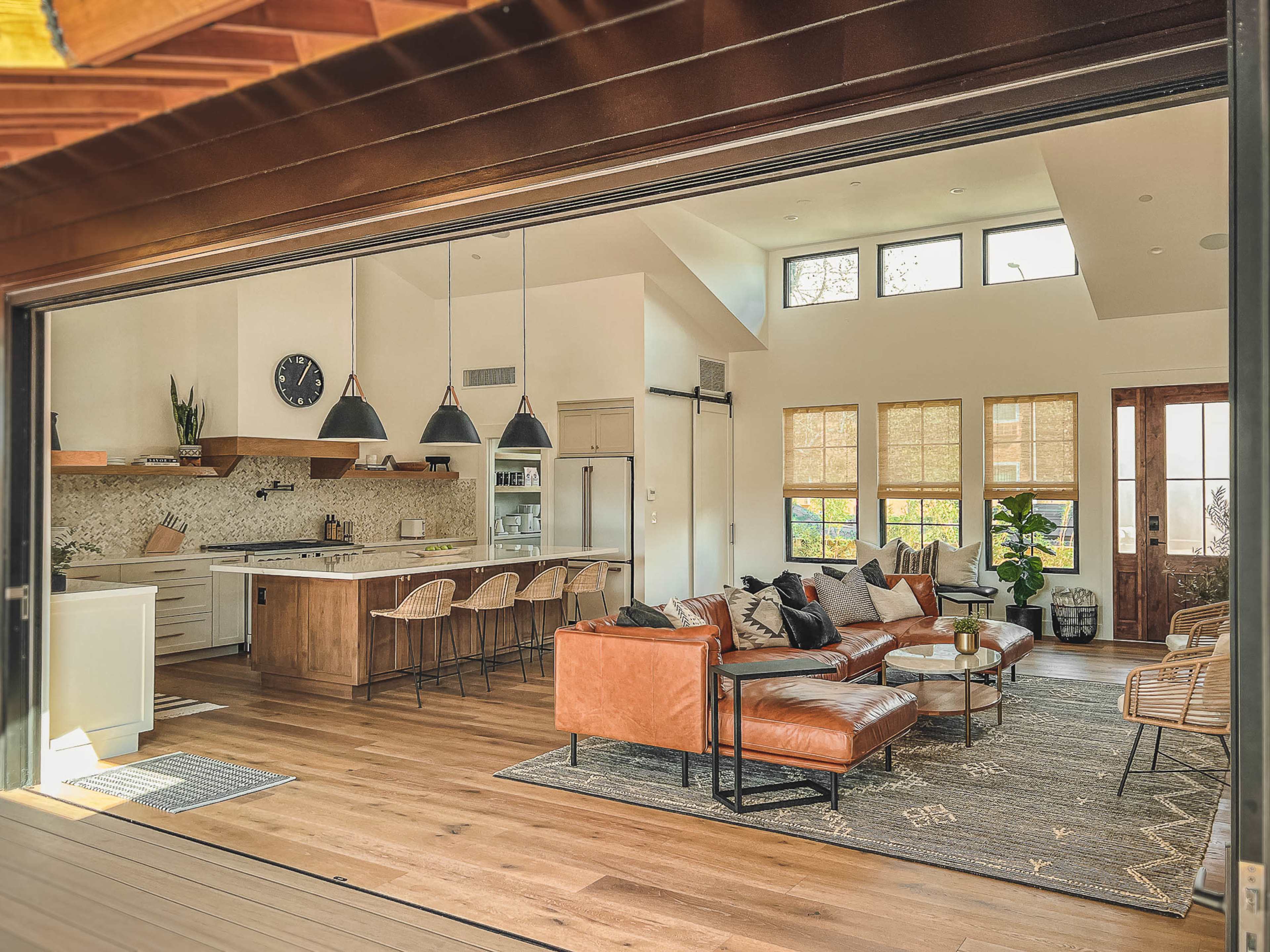 A modern living room and kitchen area with large windows, wooden flooring, and contemporary furniture.