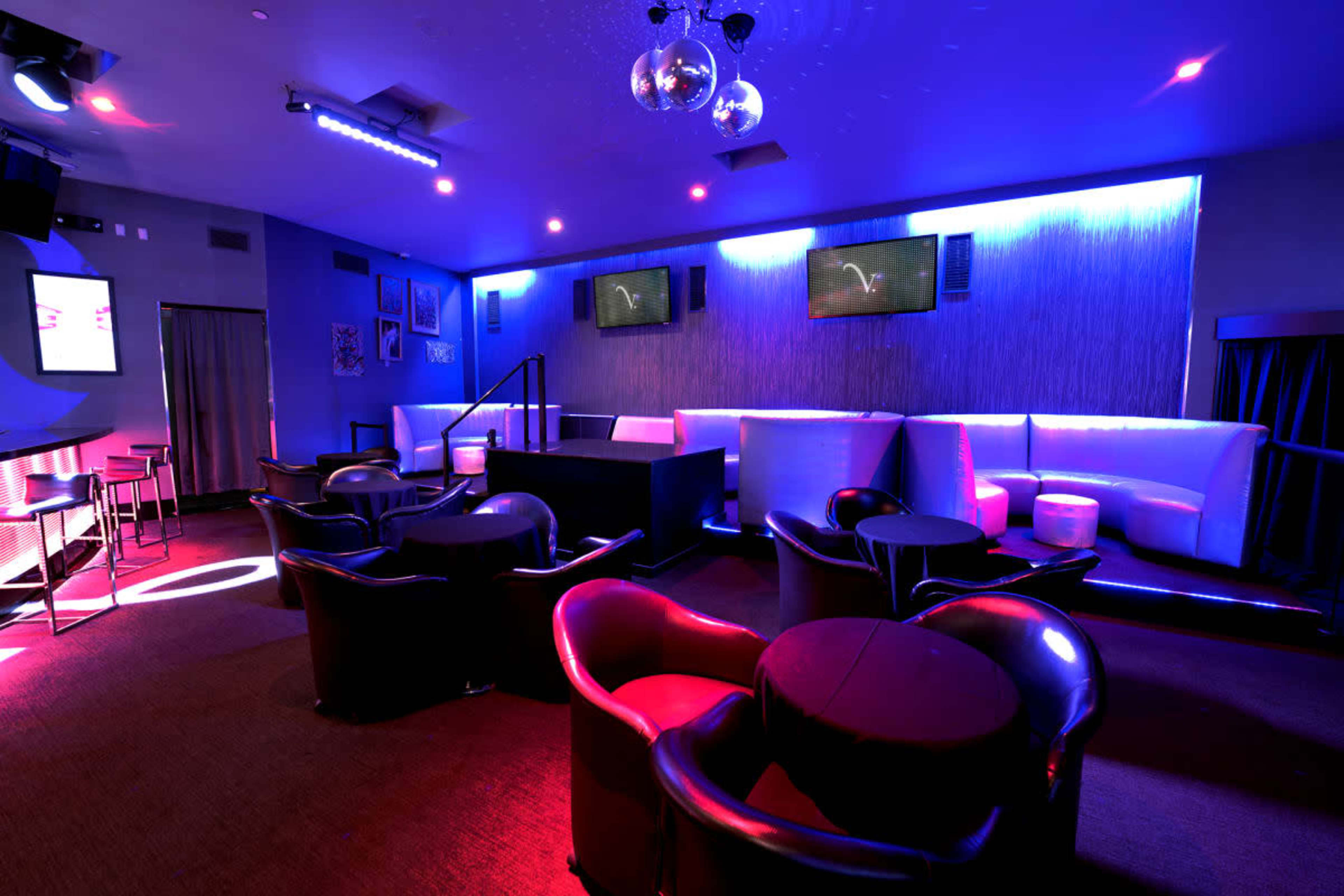 The image shows a dimly lit lounge with modern seating arrangements and colorful LED lighting.
