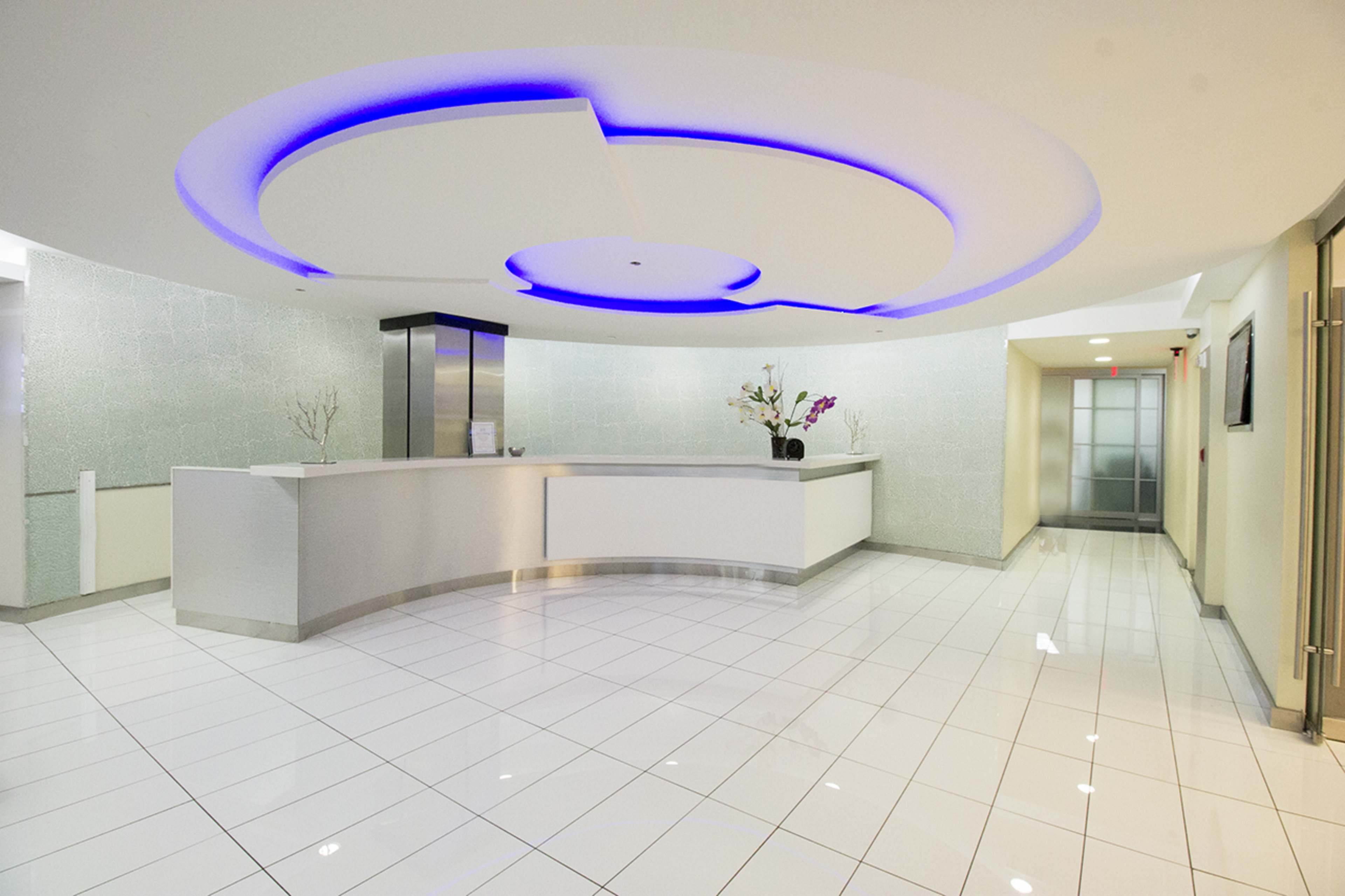 A modern reception area features a curved front desk, white tiled floors, and ambient blue lighting.