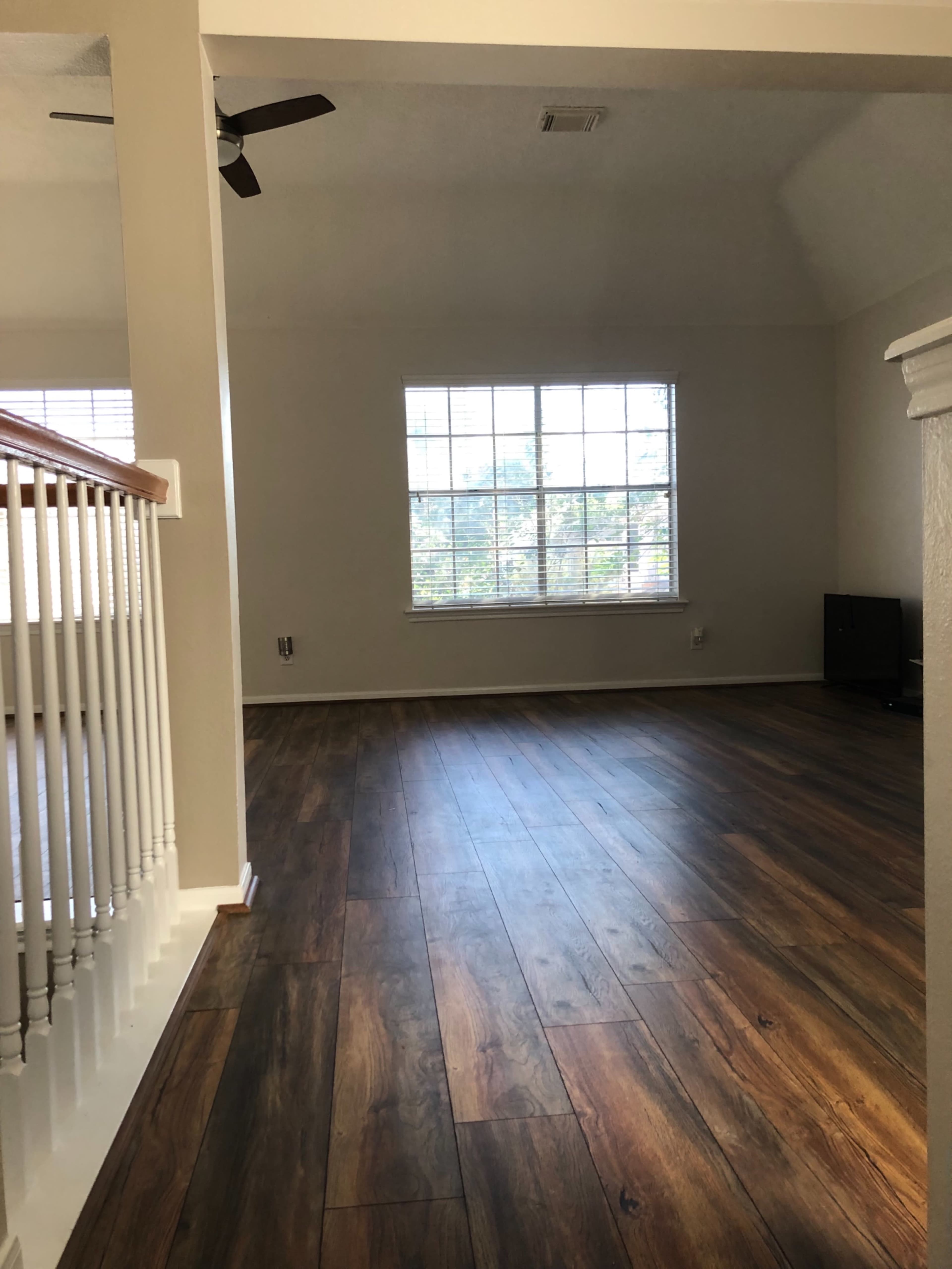 A spacious, empty room with hardwood flooring and a large window allowing natural light to enter.