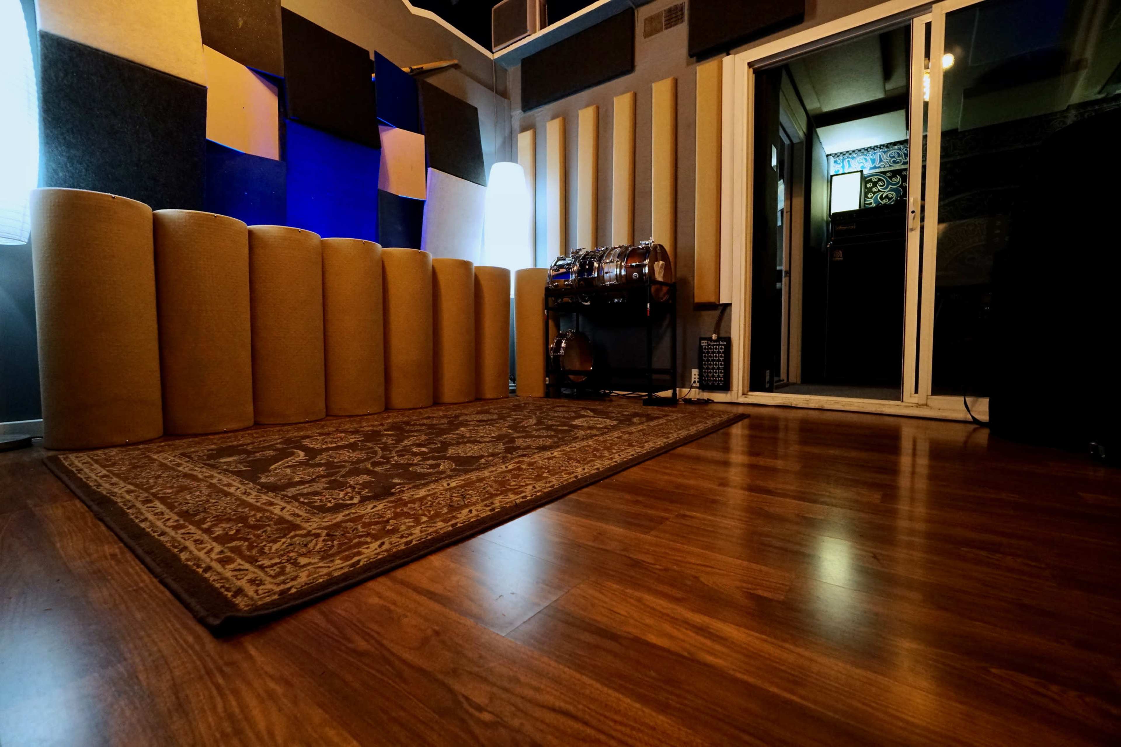 A music recording studio featuring soundproofing panels, a patterned rug on a wooden floor, and a doorway leading outside.