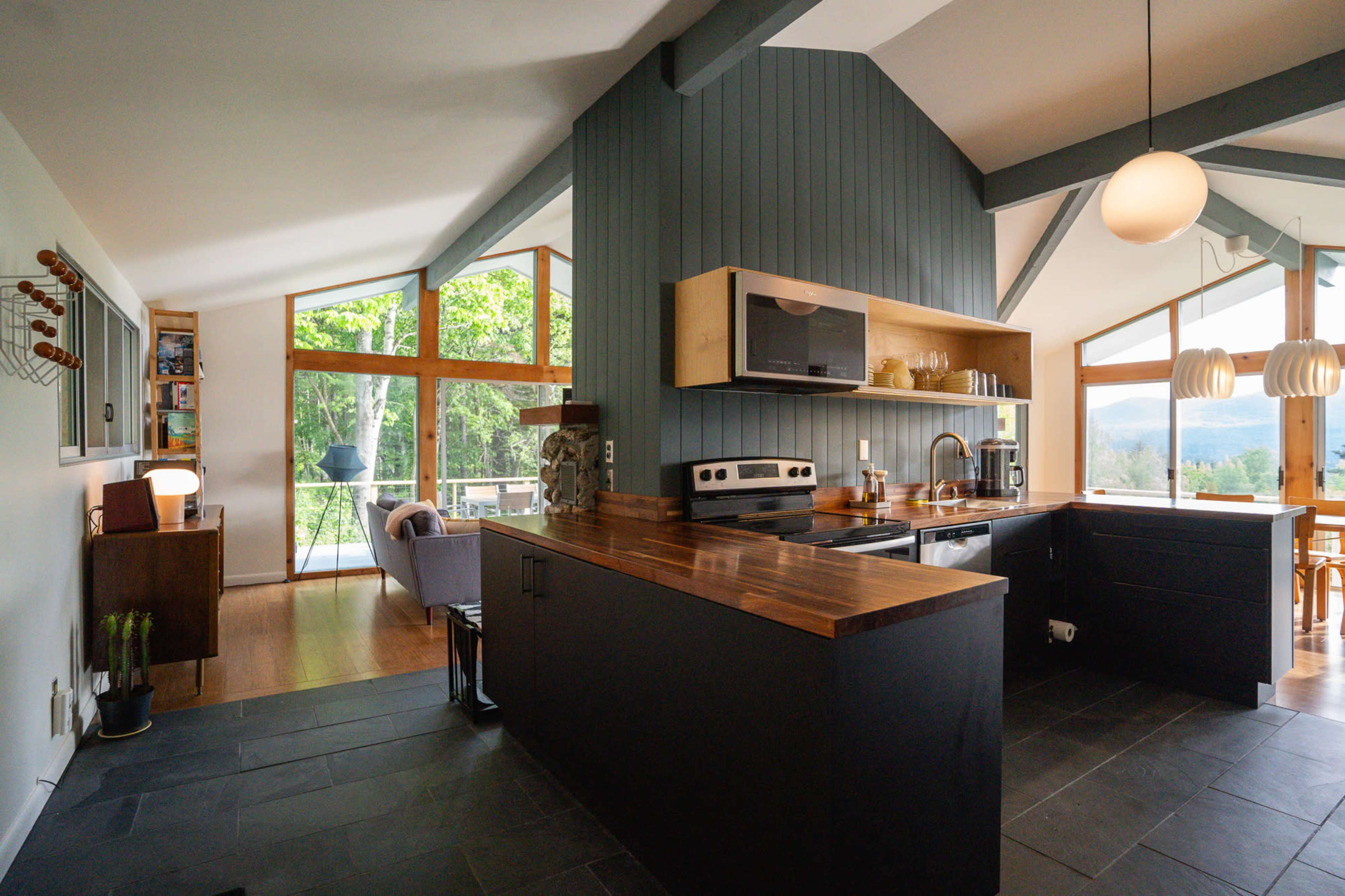 A modern kitchen features dark cabinetry, a wooden countertop, and large windows that provide a view of the outdoors.