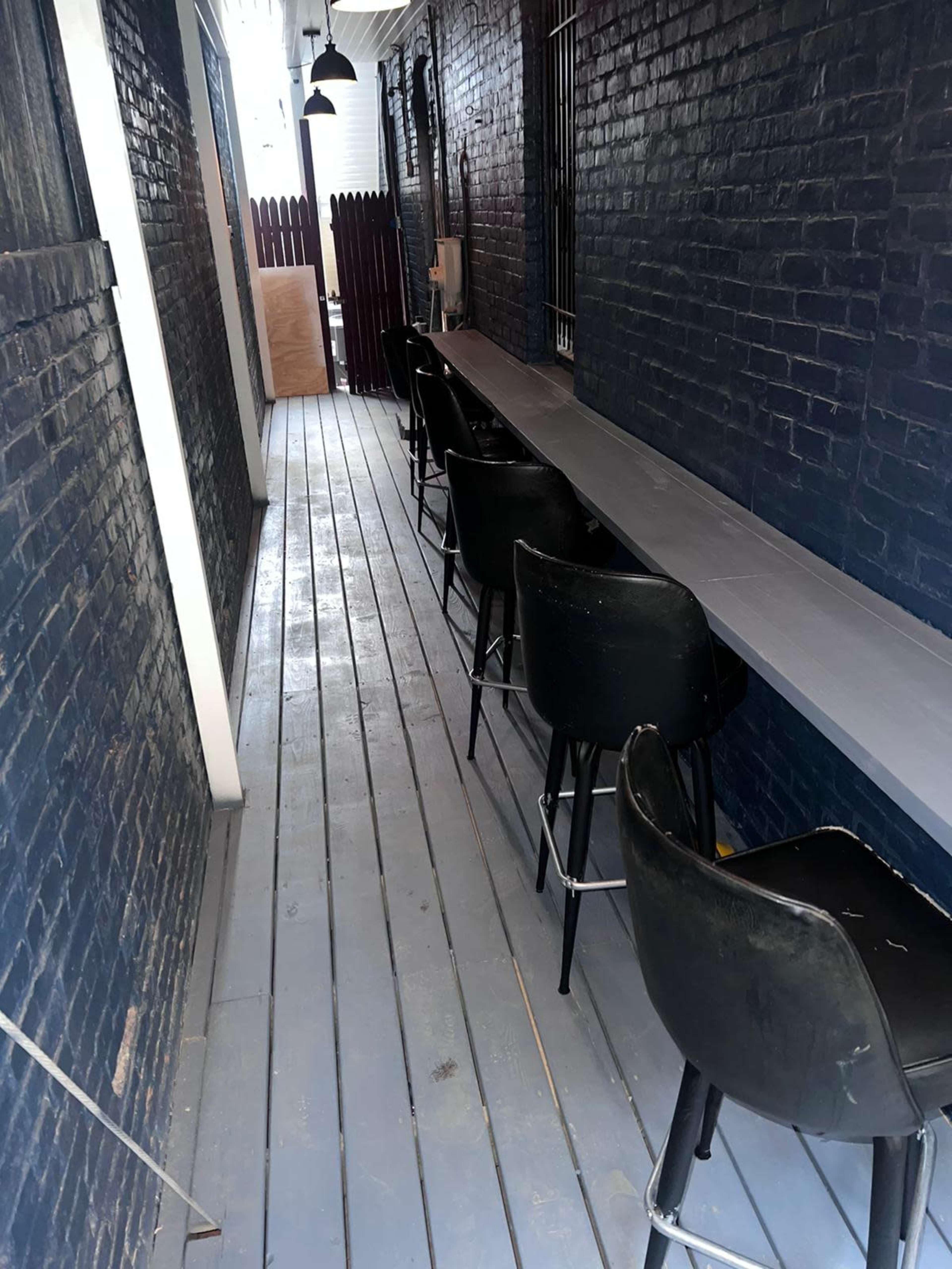 A narrow, dimly lit corridor with a row of black bar stools along a long gray counter against a dark brick wall.