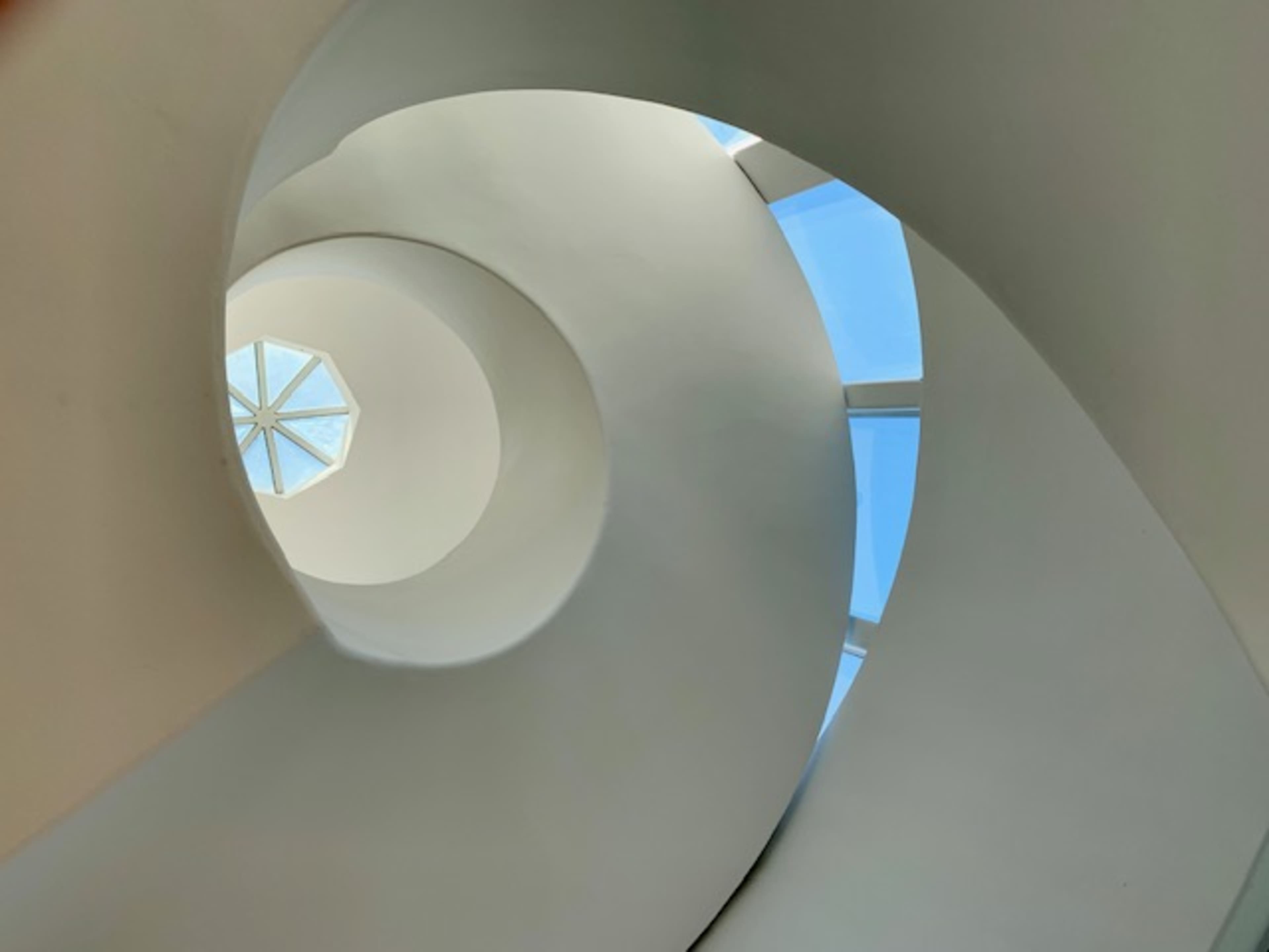 A spiral staircase ascending towards a skylight with a geometric window design.