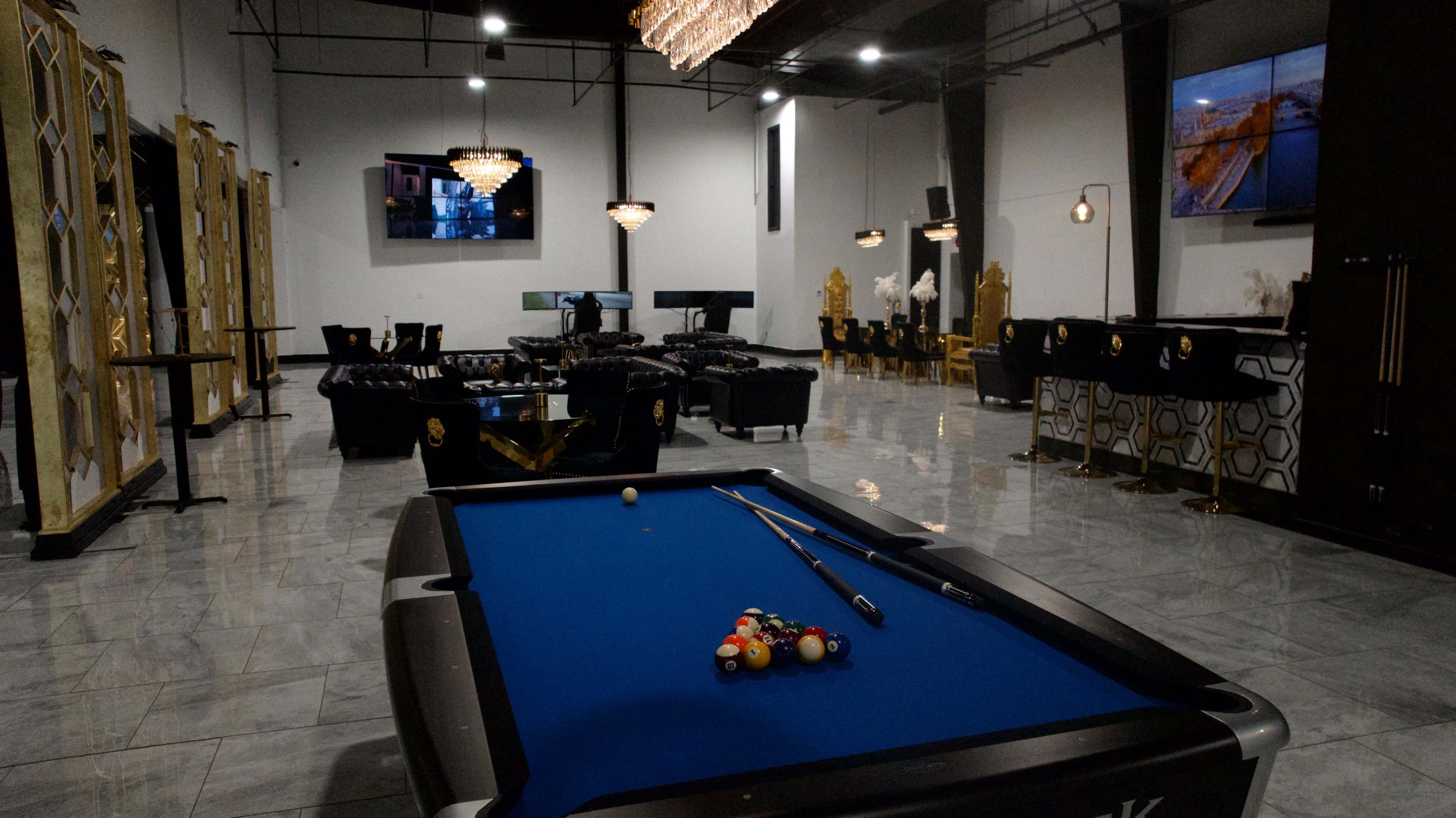 The image shows a modern lounge area featuring a pool table with balls arranged in a triangular formation, surrounded by elegant seating and decorative elements.