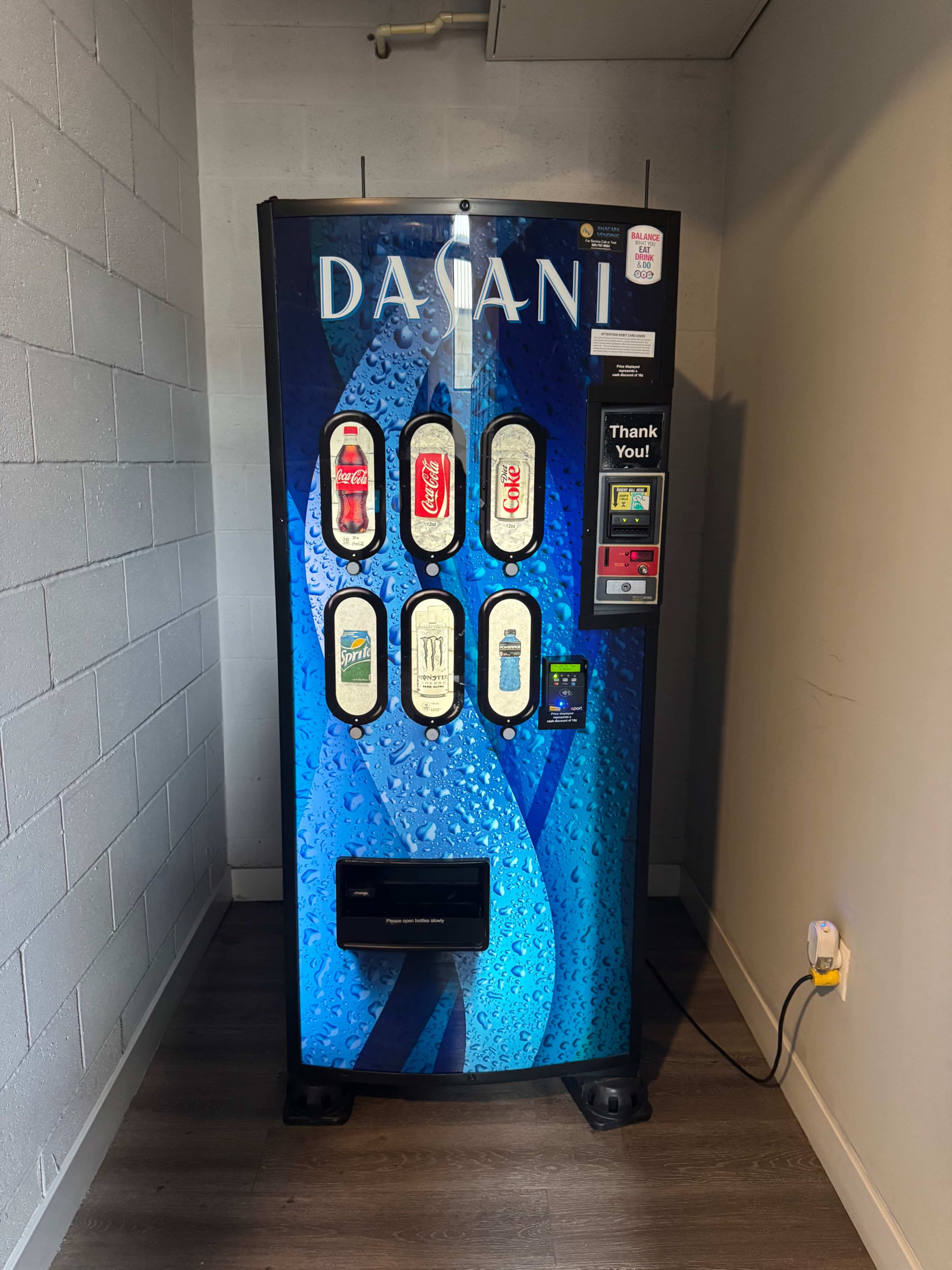 The image shows a vending machine displaying various beverage options, including soda and water, against a blue background.