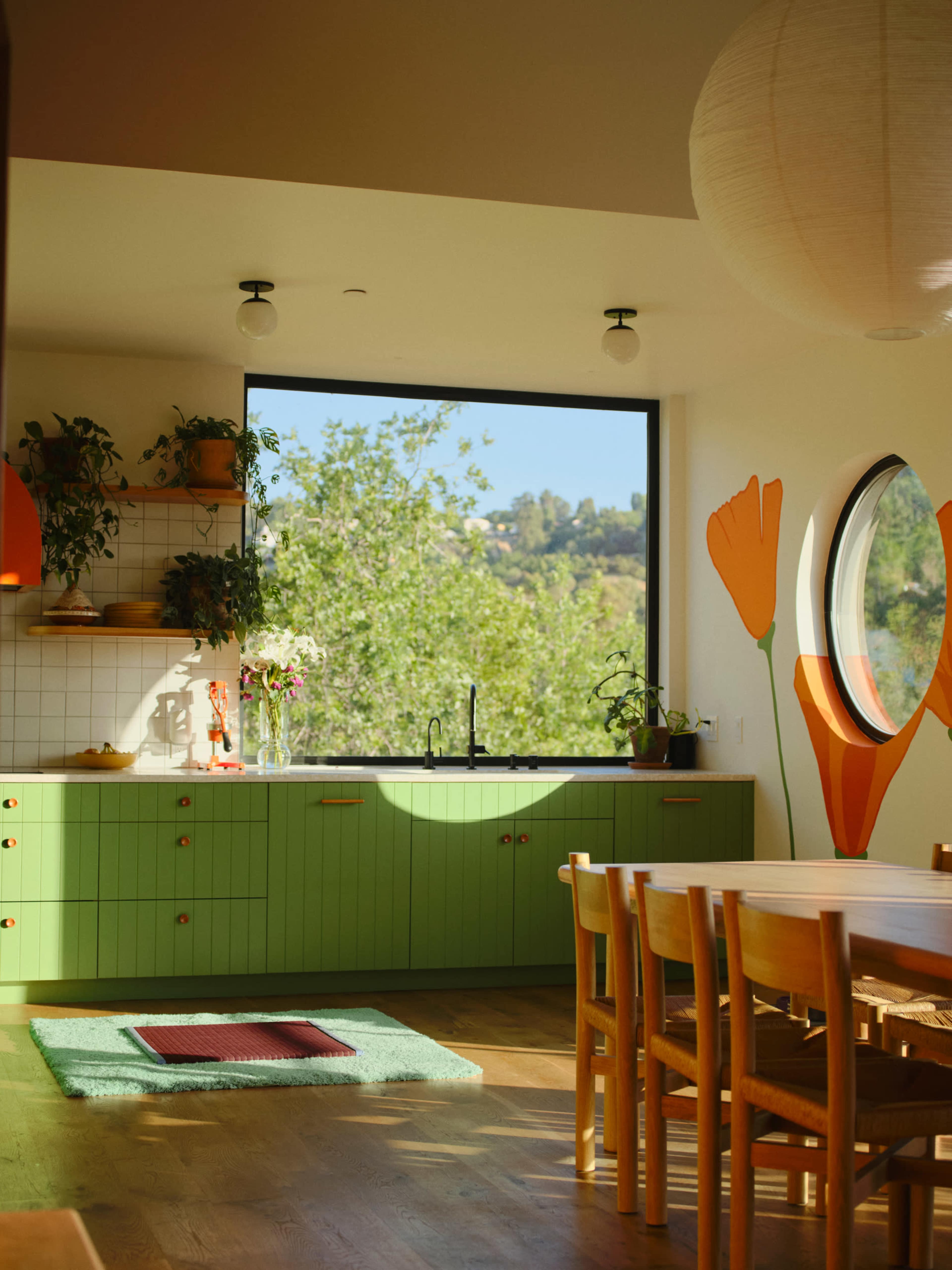 The image shows a modern kitchen featuring green cabinetry, a circular window, and a dining area with a wooden table.