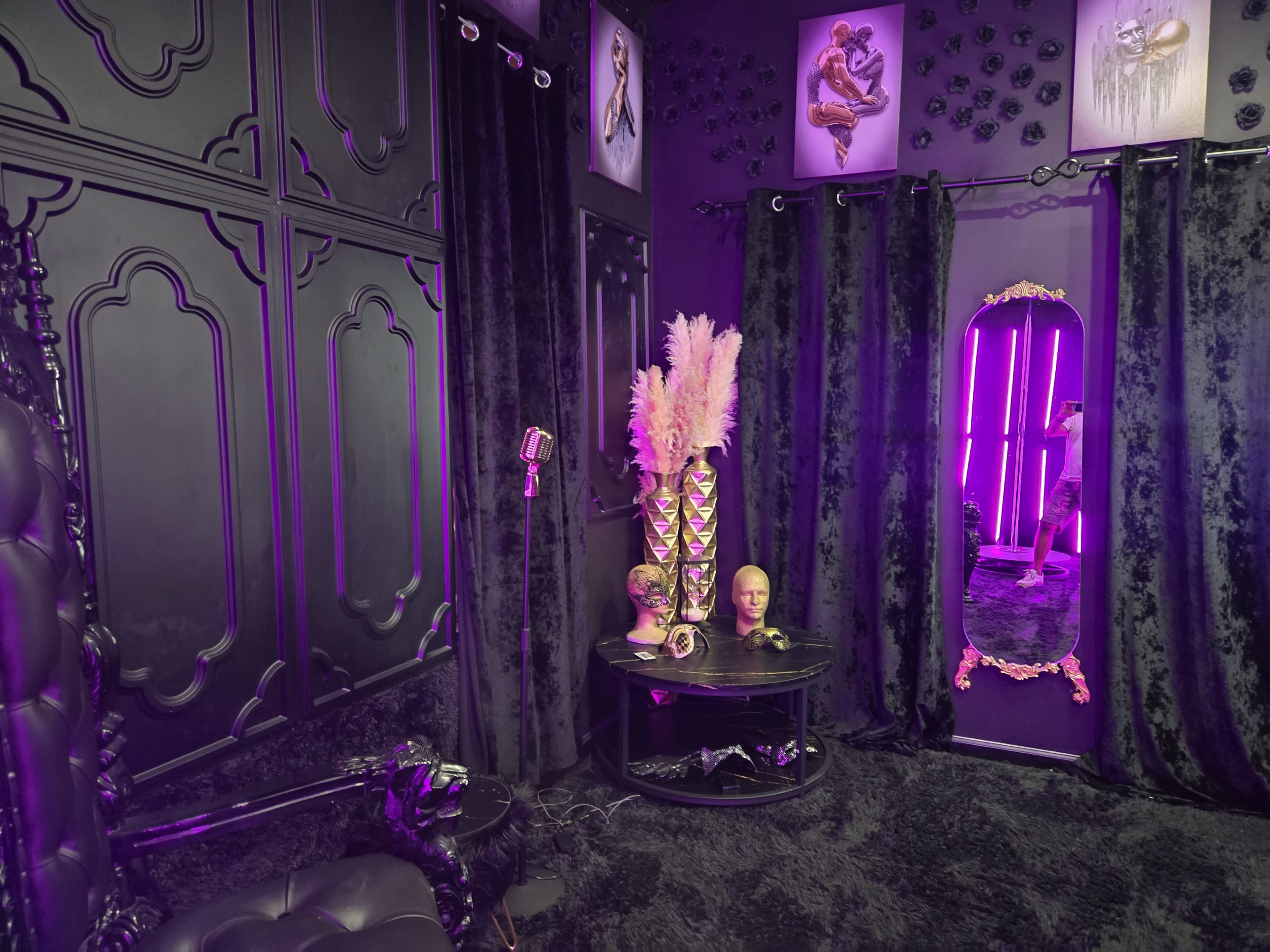 The image shows a dimly lit room with black walls, plush velvet curtains, and decorative elements including a mirrored vanity and floral arrangements.