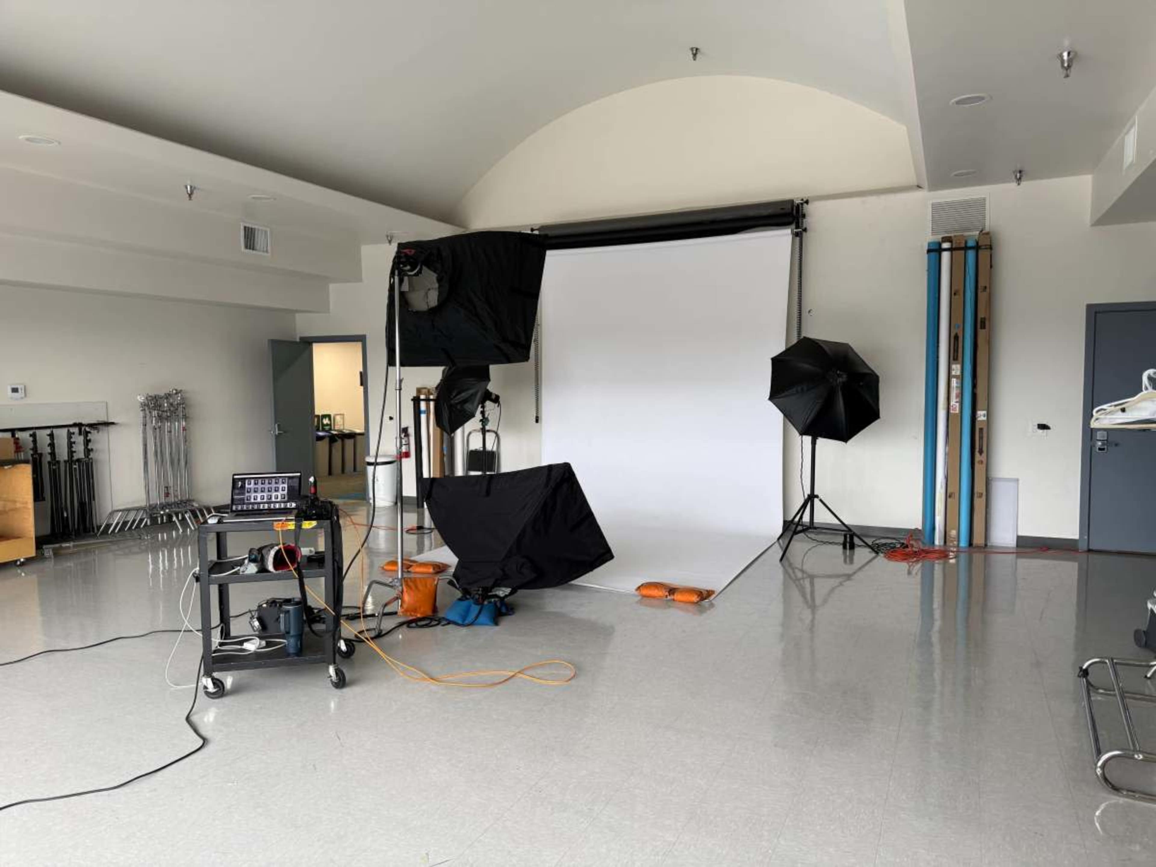 The image shows a photography studio setup with a backdrop, lighting equipment, and a mobile cart in an empty room.