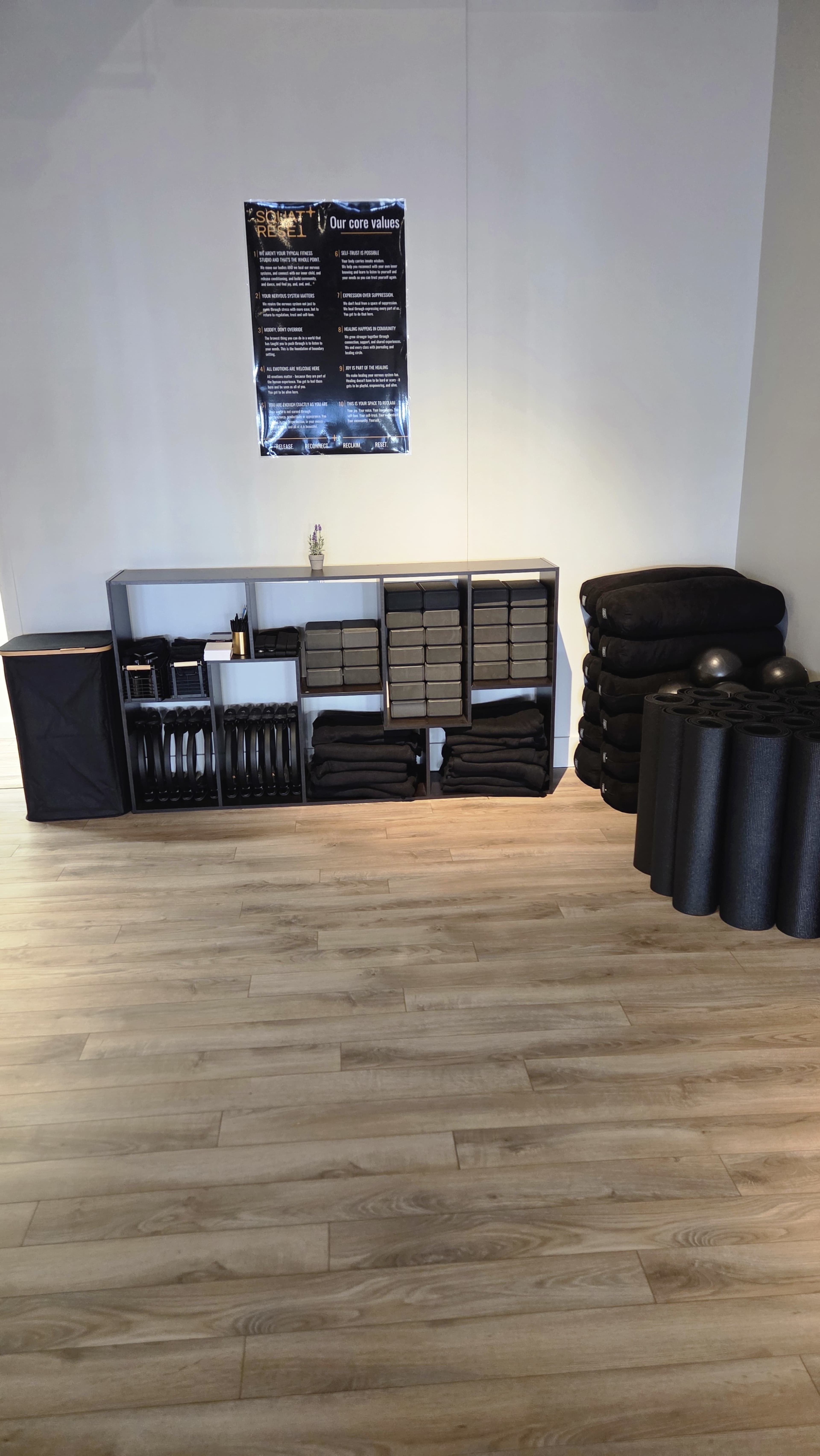 The image shows a neatly organized interior space featuring shelves with folded items, storage bins, and exercise mats, all arranged on a wooden floor.