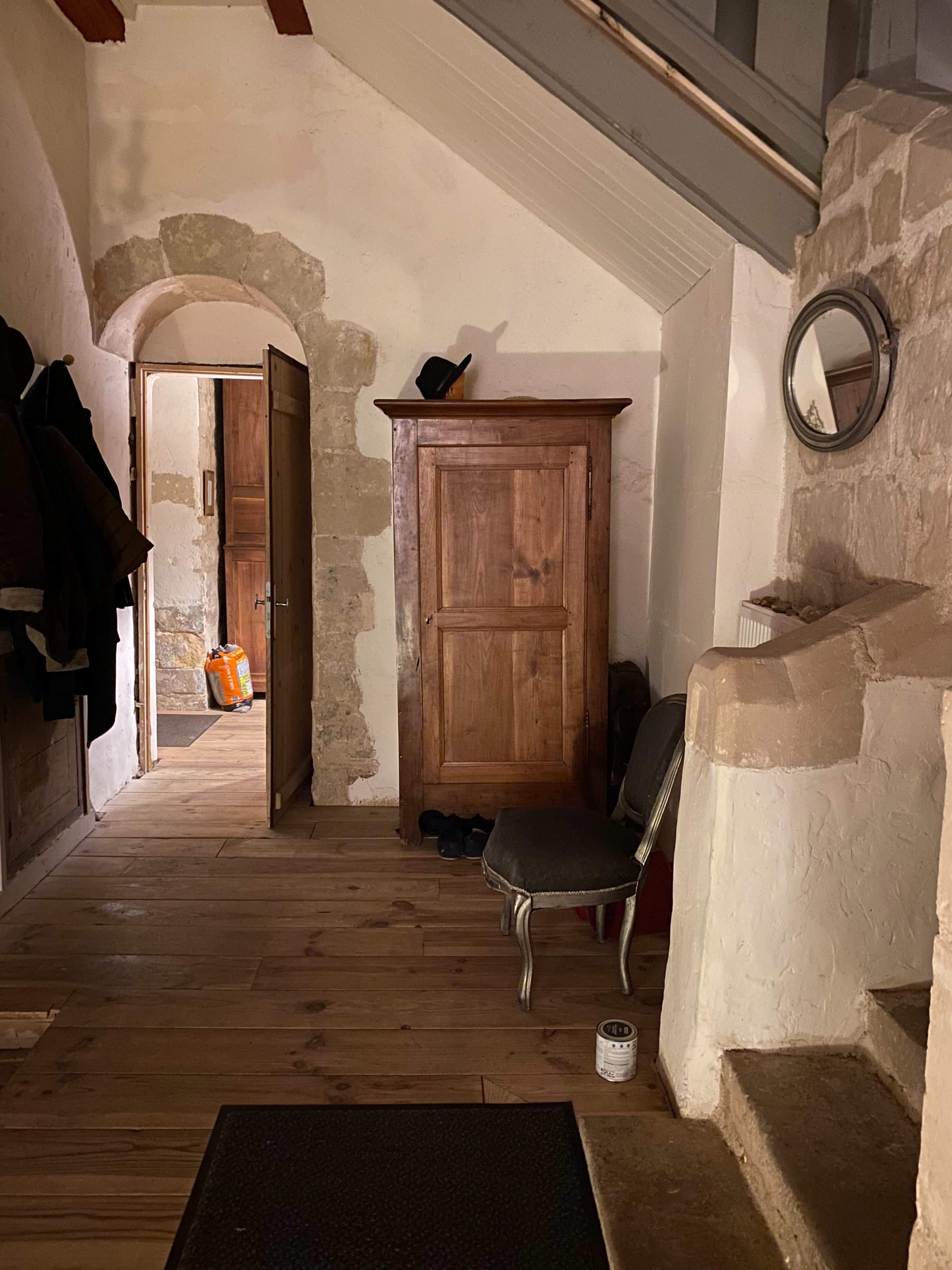 A wooden cabinet stands against a wall in a dimly lit entryway, with a staircase visible at the top and a door leading to another room in the background.