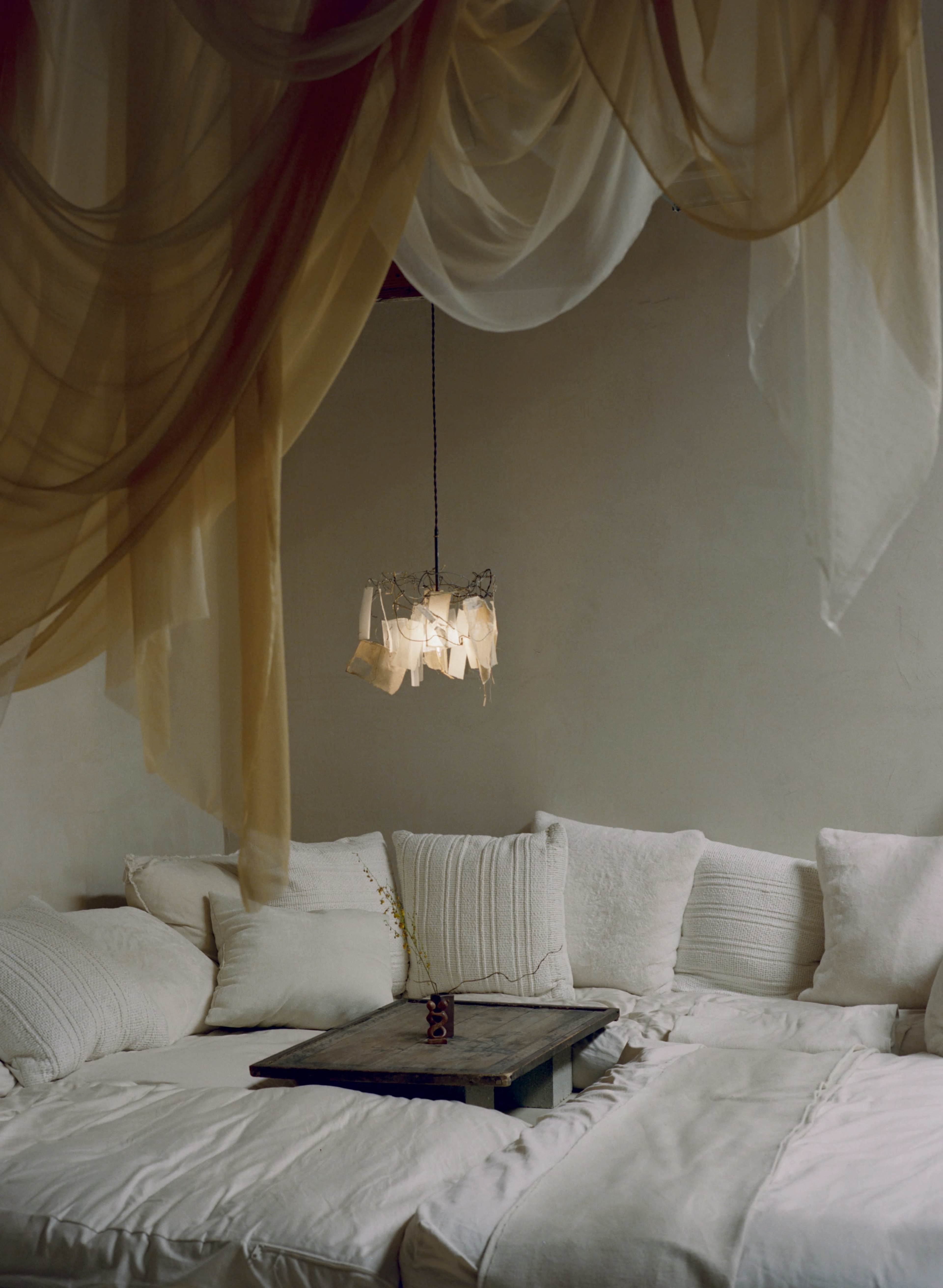 A cozy seating area is adorned with soft white cushions and a unique hanging light fixture above a wooden table.