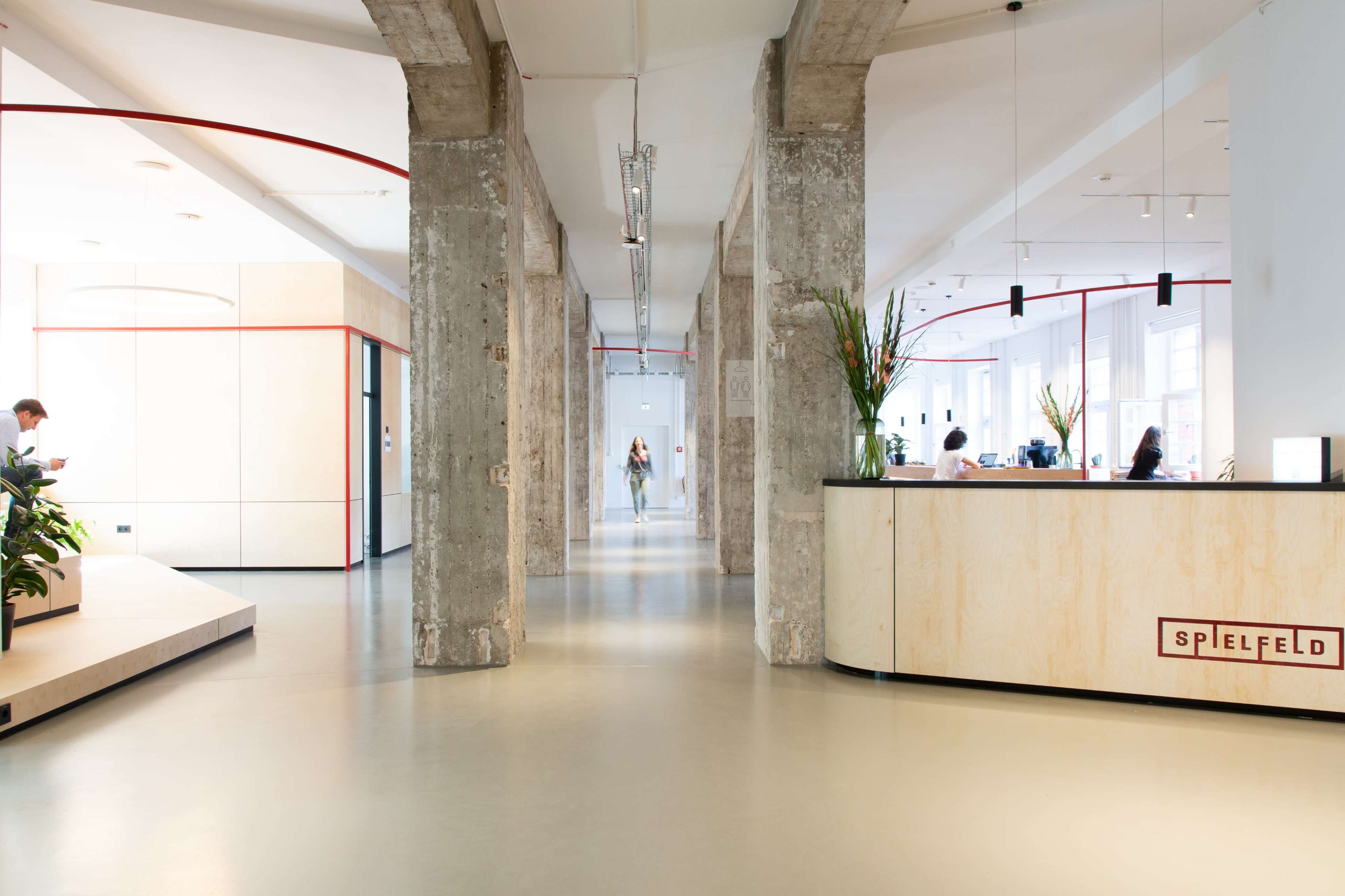 A modern office interior with large windows, concrete pillars, and a reception desk labeled "SPIELFELD."