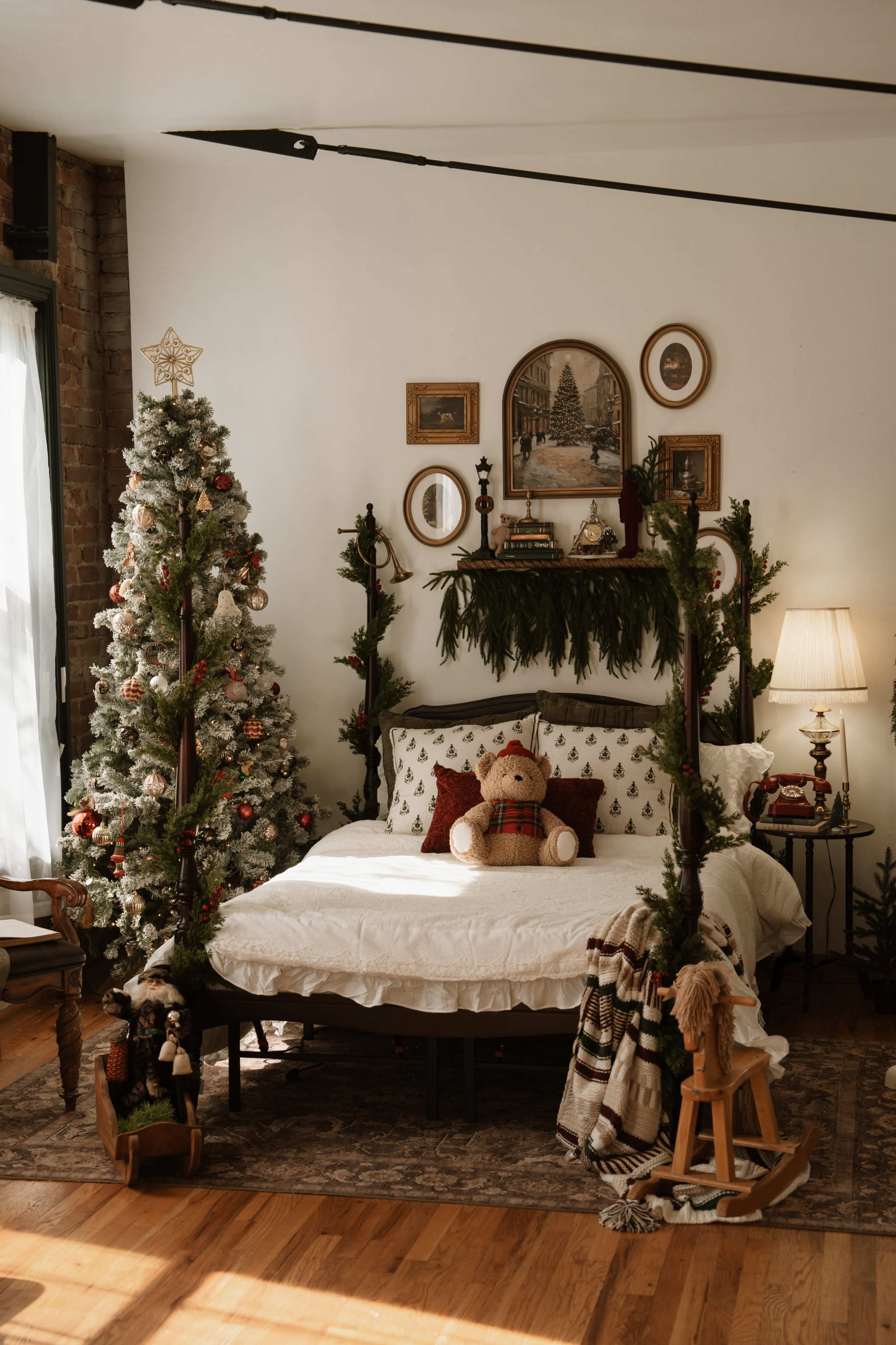 The image shows a cozy bedroom decorated for Christmas, featuring a bed with white bedding, a Christmas tree adorned with ornaments, and seasonal decorations on the walls and furniture.