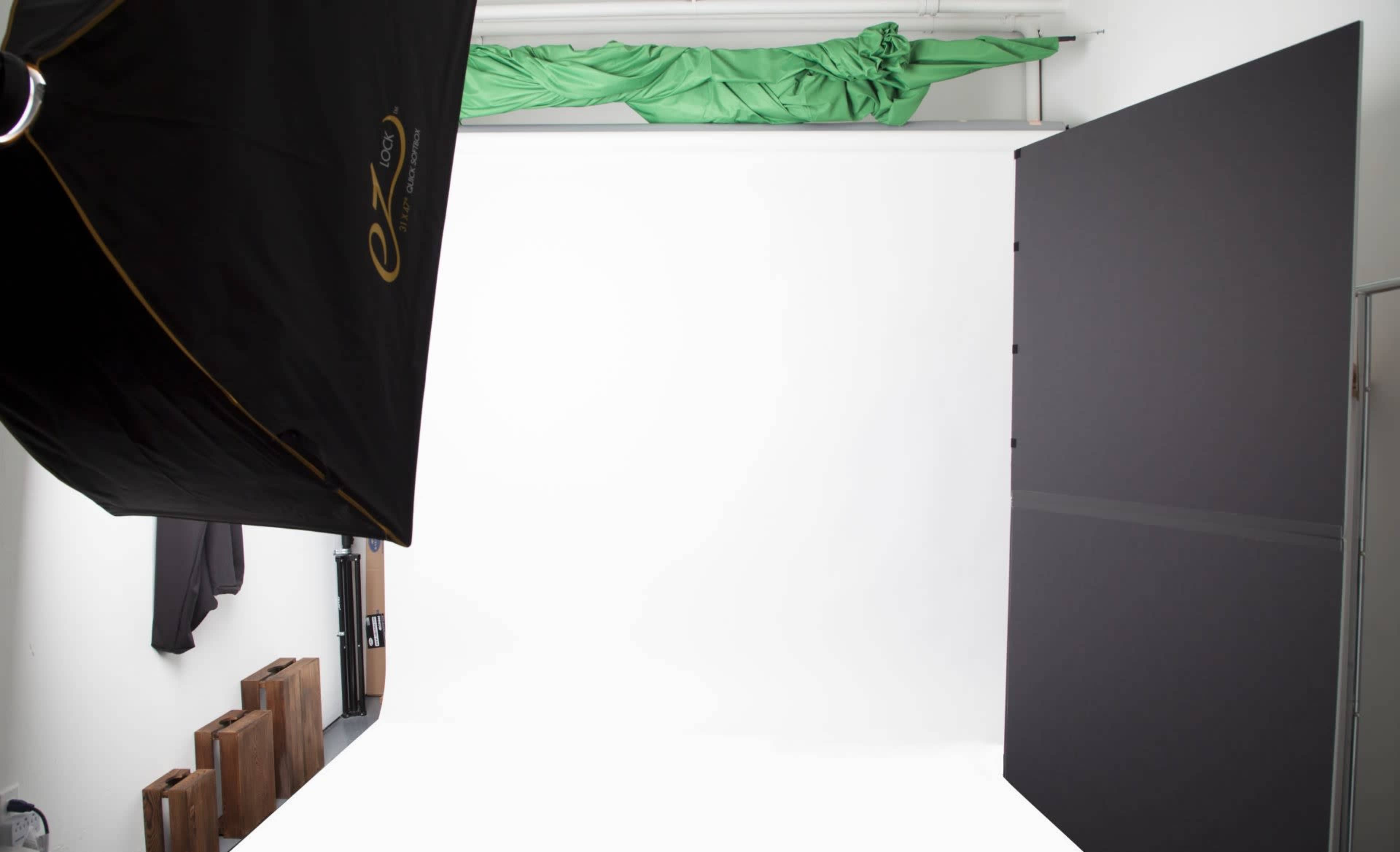 The image shows a photography studio with a white backdrop, softbox lighting, and a piece of green fabric draped on the ceiling.