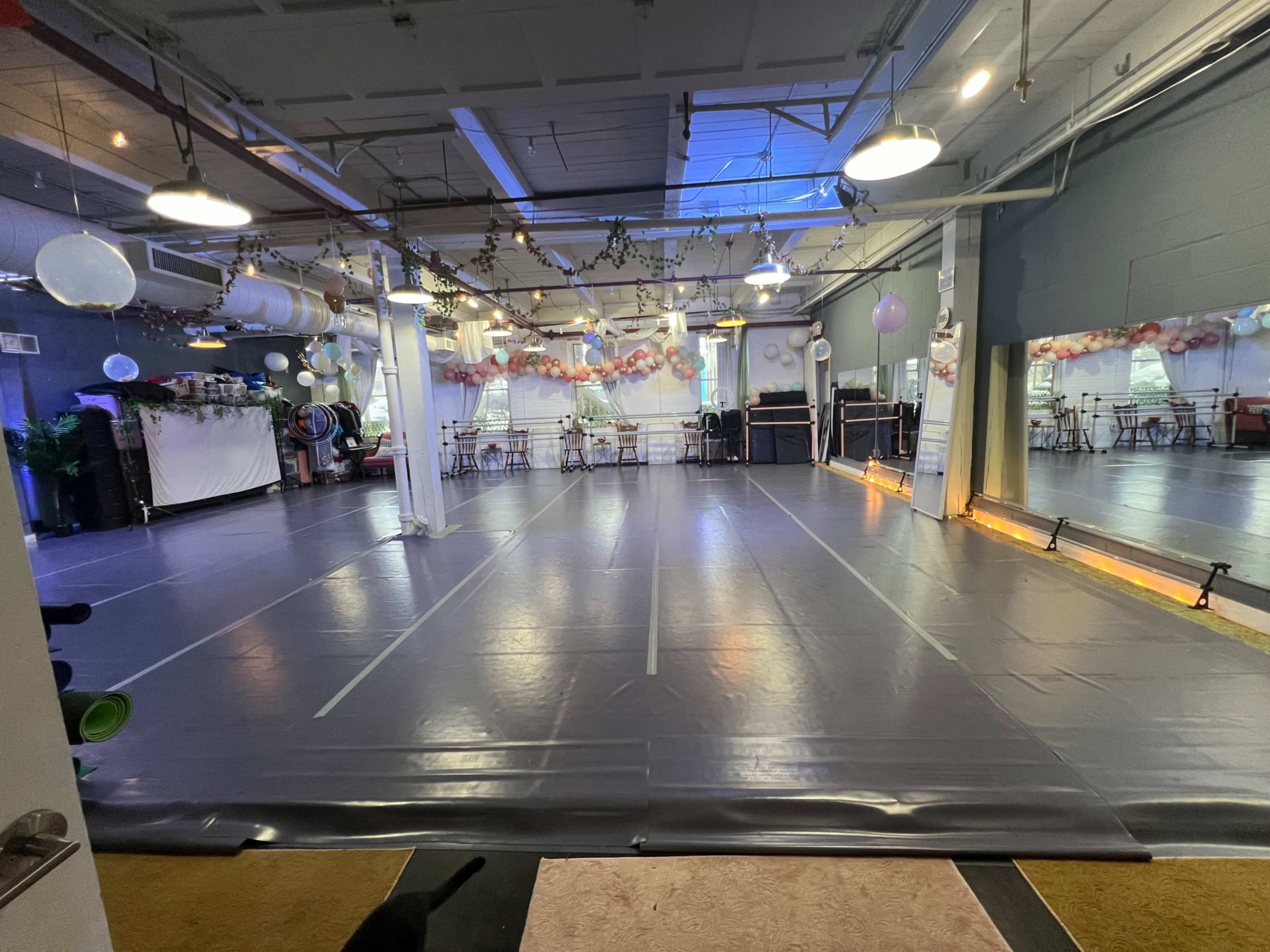 A spacious dance studio with a shiny floor, decorated with balloons and set up for an event.