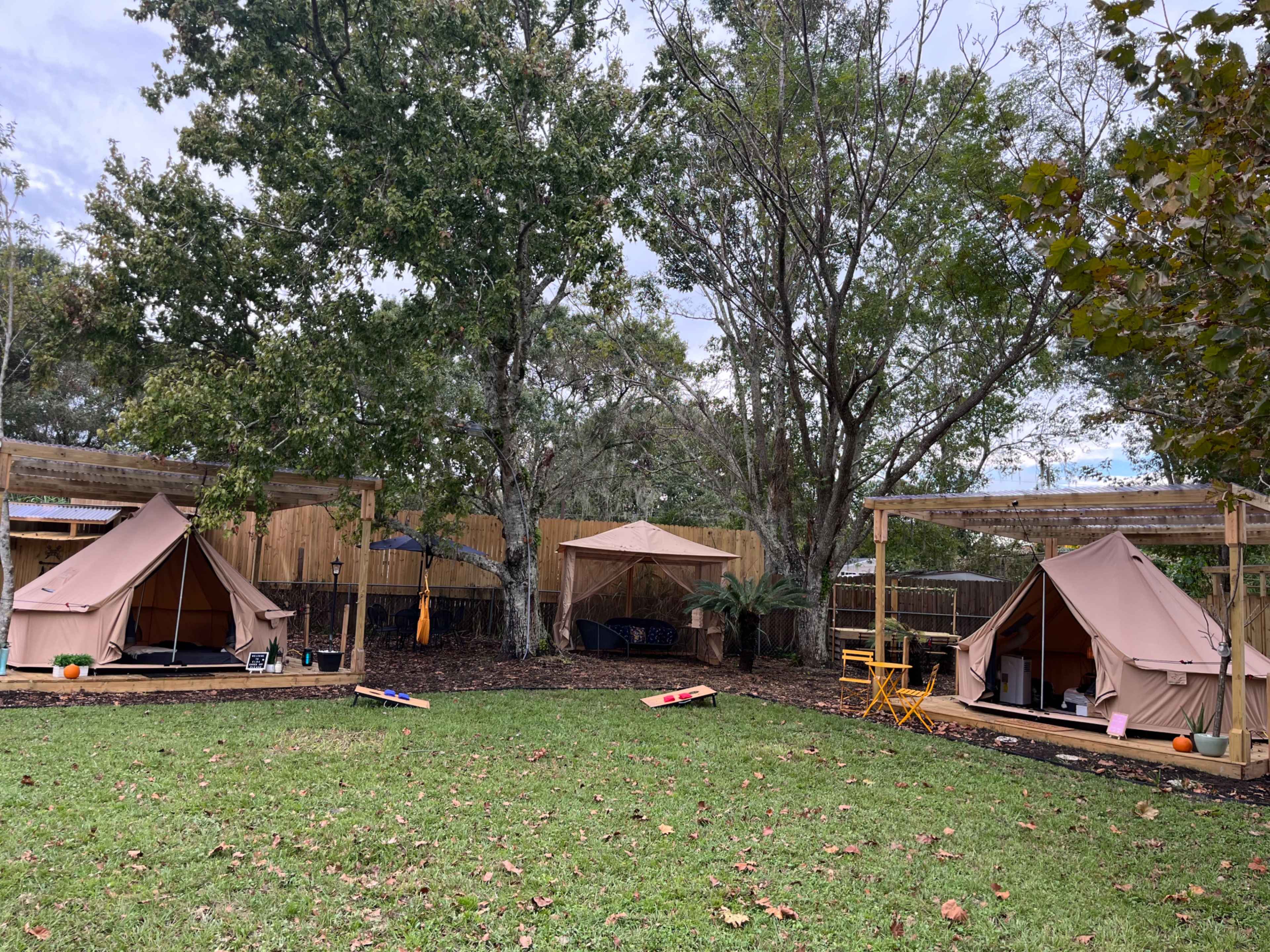 A glamping site featuring three canvas tents arranged in a grassy area surrounded by trees and wooden fencing.