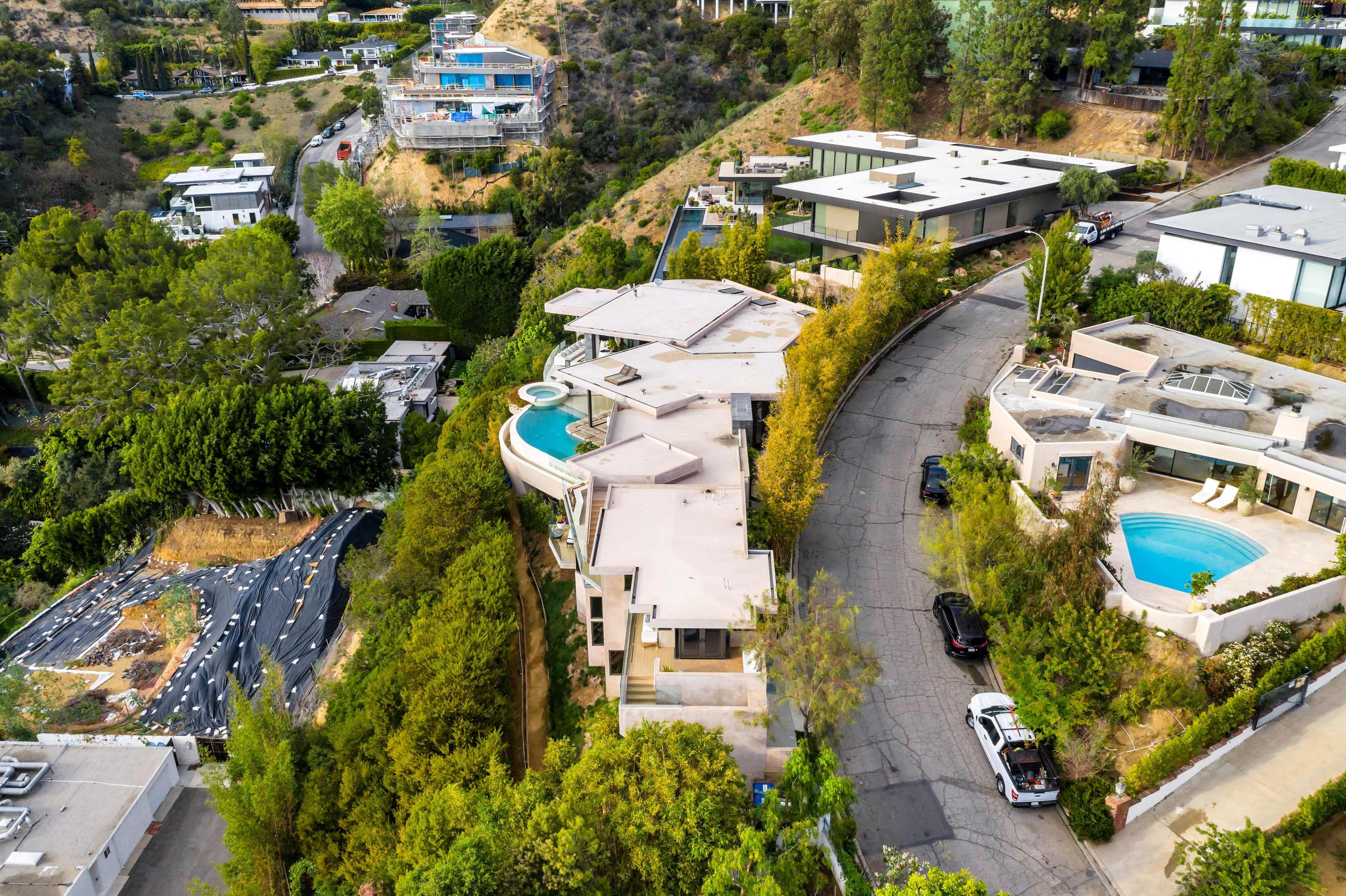 A curved road lined with modern homes, with one house featuring a swimming pool and another with a distinct circular driveway on a hillside.
