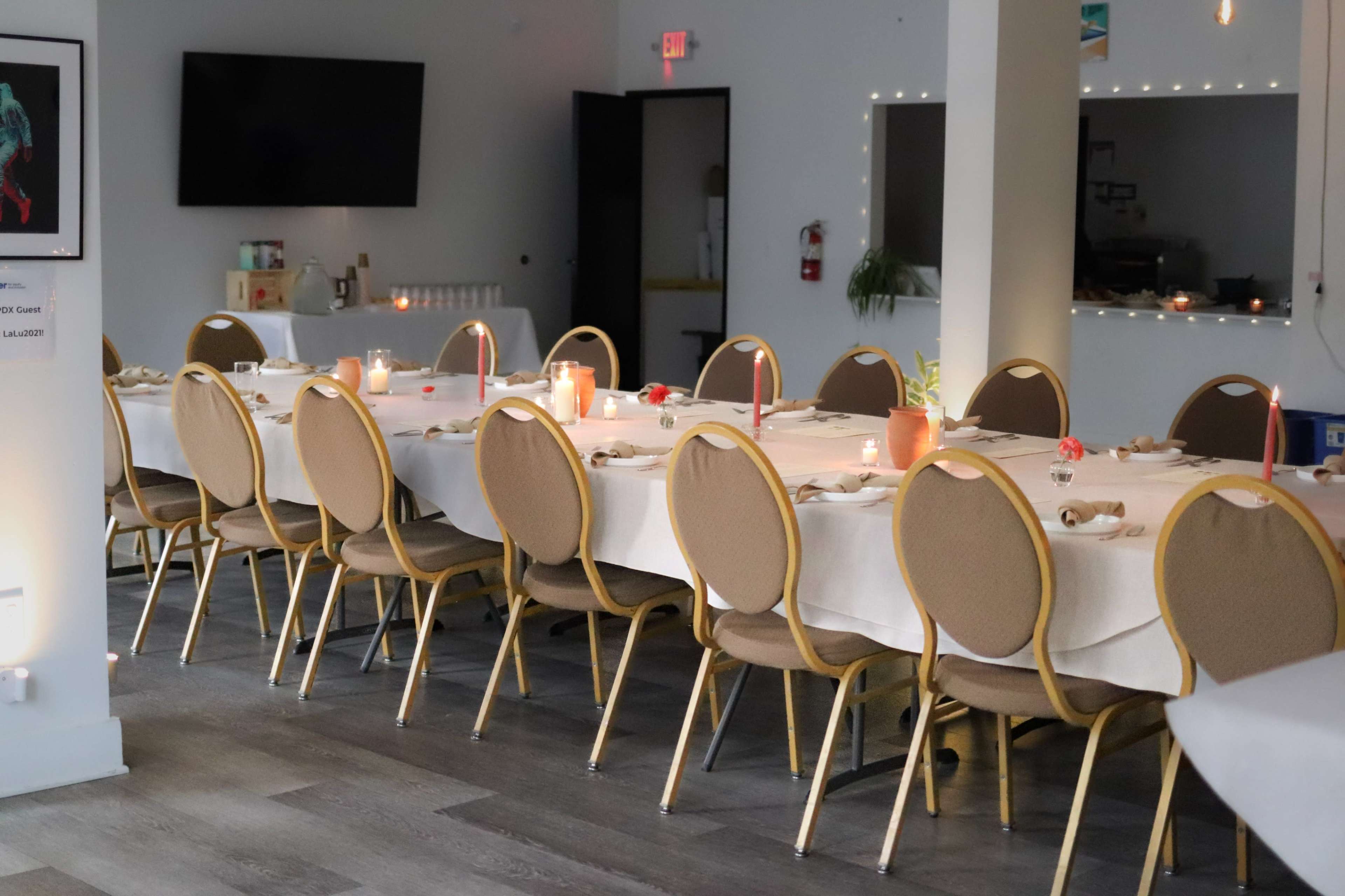 A long, elegantly set dining table with chairs is arranged in a well-lit, spacious room featuring a screen and soft lighting.